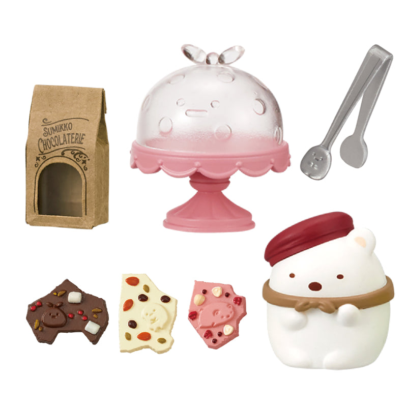 SUMIKKO CHOCOLATERIE Re-ment Blind Box Series featuring a chocolate-making playset with cake stand, chocolate bars, Shirokuma figurine, tongs, and kraft-paper bag.