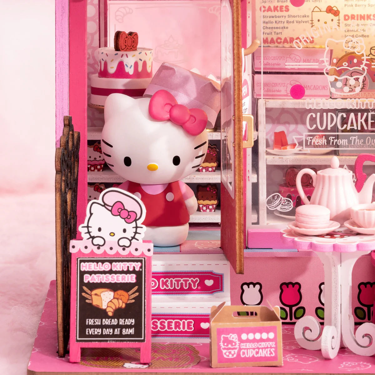Hello Kitty Patisserie diorama with Hello Kitty figure, glass display of pastries, chalkboard sign, take-out box, and tea set on sidewalk.