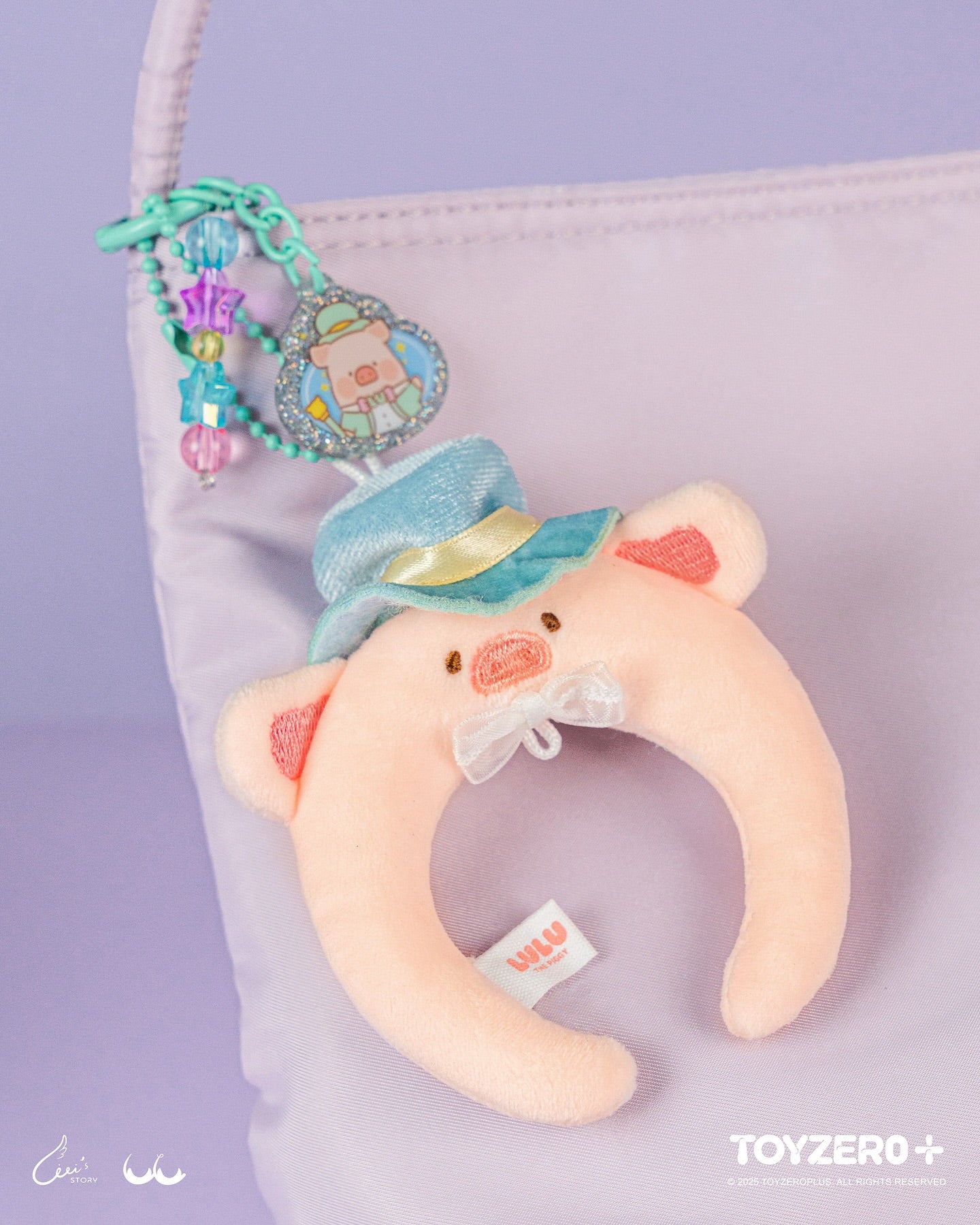 LuLu the Piggy LuLuLand - Magician Lu Headband Plush Keychain features a crescent-shaped pig charm with a teal hat and bow, clipped onto a lavender purse.