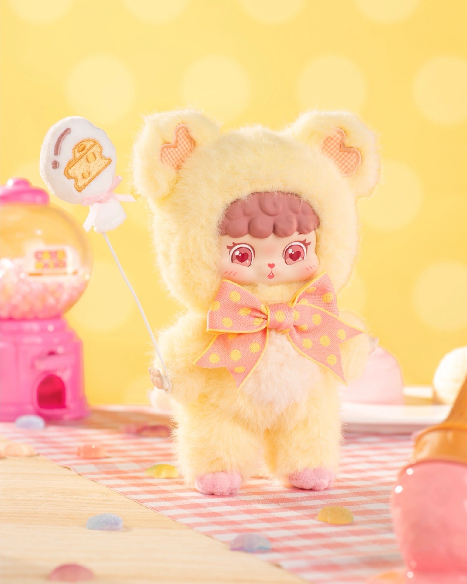 Puffynose Friend Memo Plush Pendant Blind Box: A toy figure in a yellow animal costume with pink heart eyes, holding a candy lollipop, on a decorative tabletop.