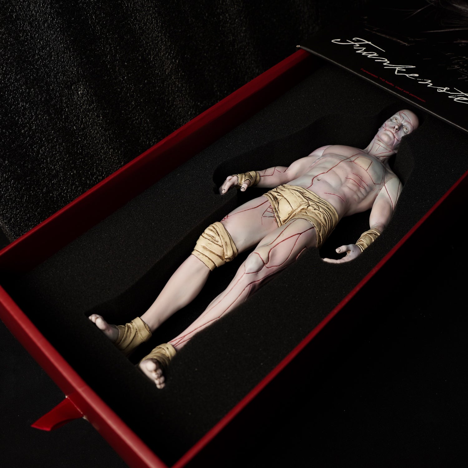 Frankenstein: The Creature V1, a 30cm soft vinyl figure with detailed anatomy and red vein lines, displayed in foam packaging within a red box.