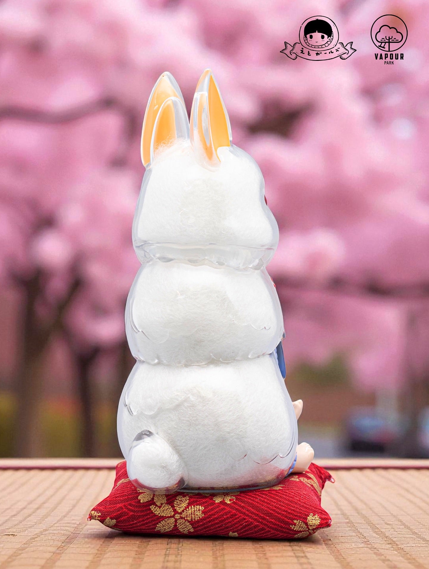 Kigurumi Bunny by Ebimomo & Vapourpark on red cushion, featuring clear vinyl with white stuffing and upright ears. Preorder for a whimsical art toy.