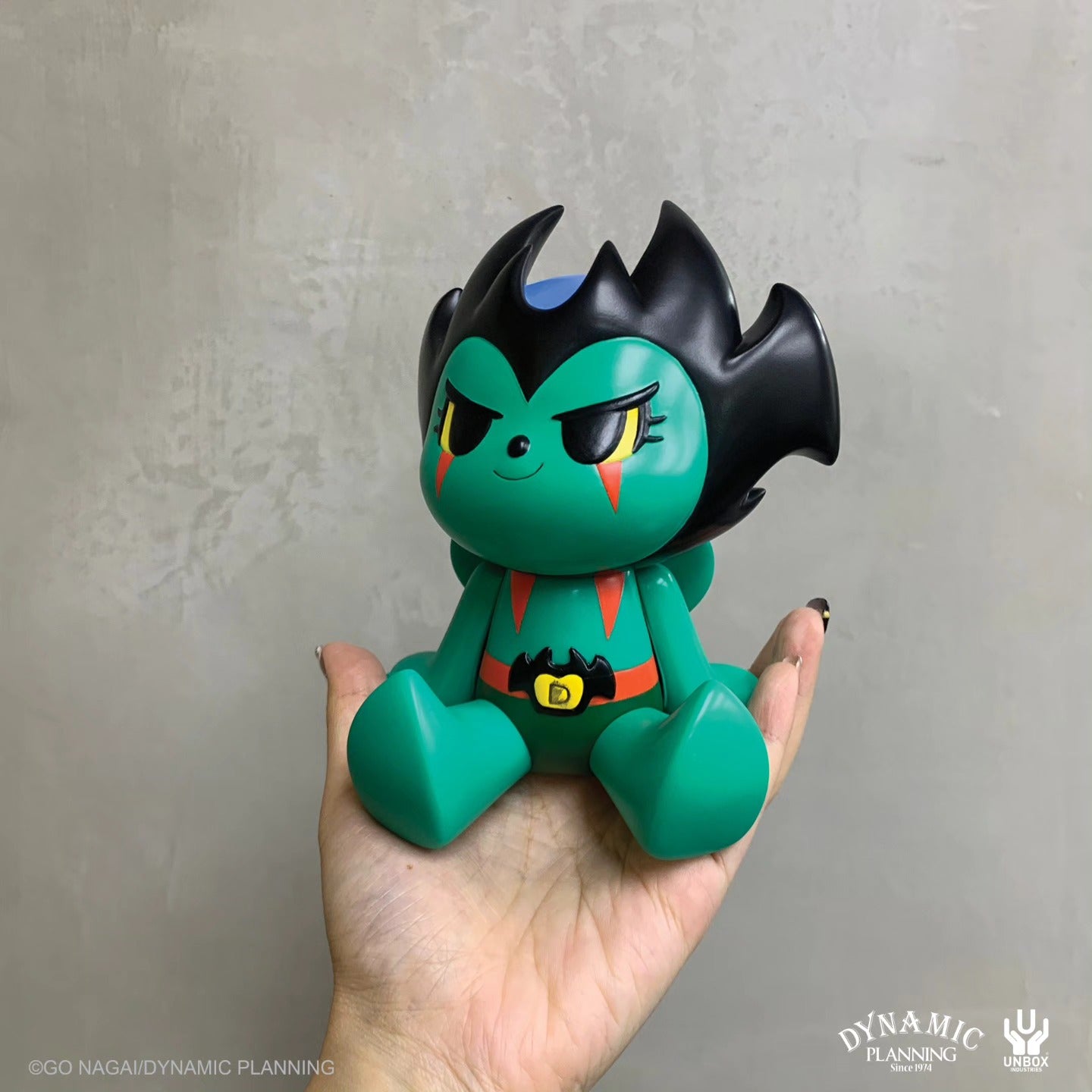Go Nagai Devilman by Too Natthapong vinyl art-toy features a green body, bat-wing hair, and bat-logo belt, held in hand, collectible from Dynamic Planning and Unbox Industries.