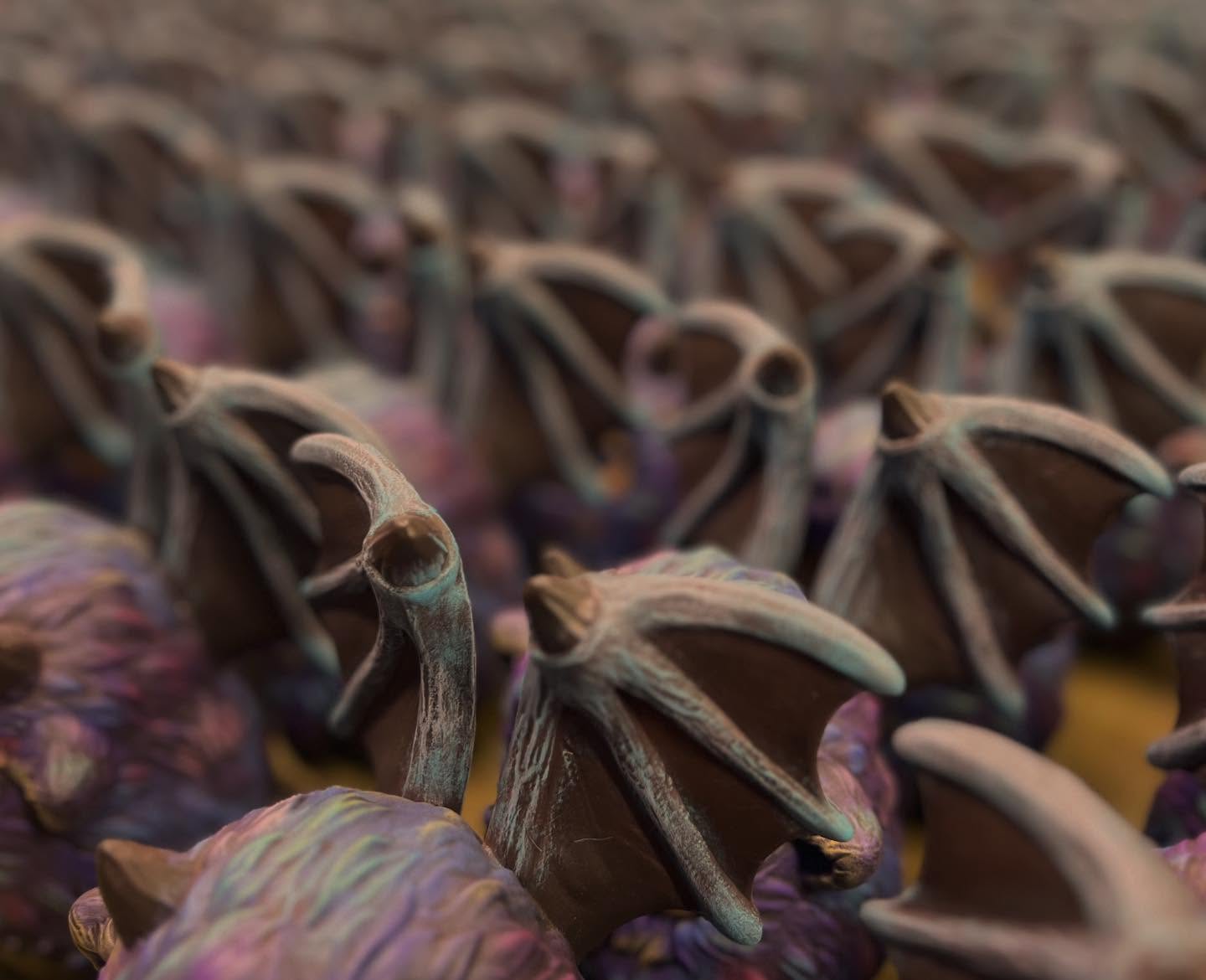 Macro shot of ZuZu Monster by Pucky, featuring rows of bat-shaped figurines with folded wings and pointed ears, dusted with iridescent coating. Limited 120 edition.
