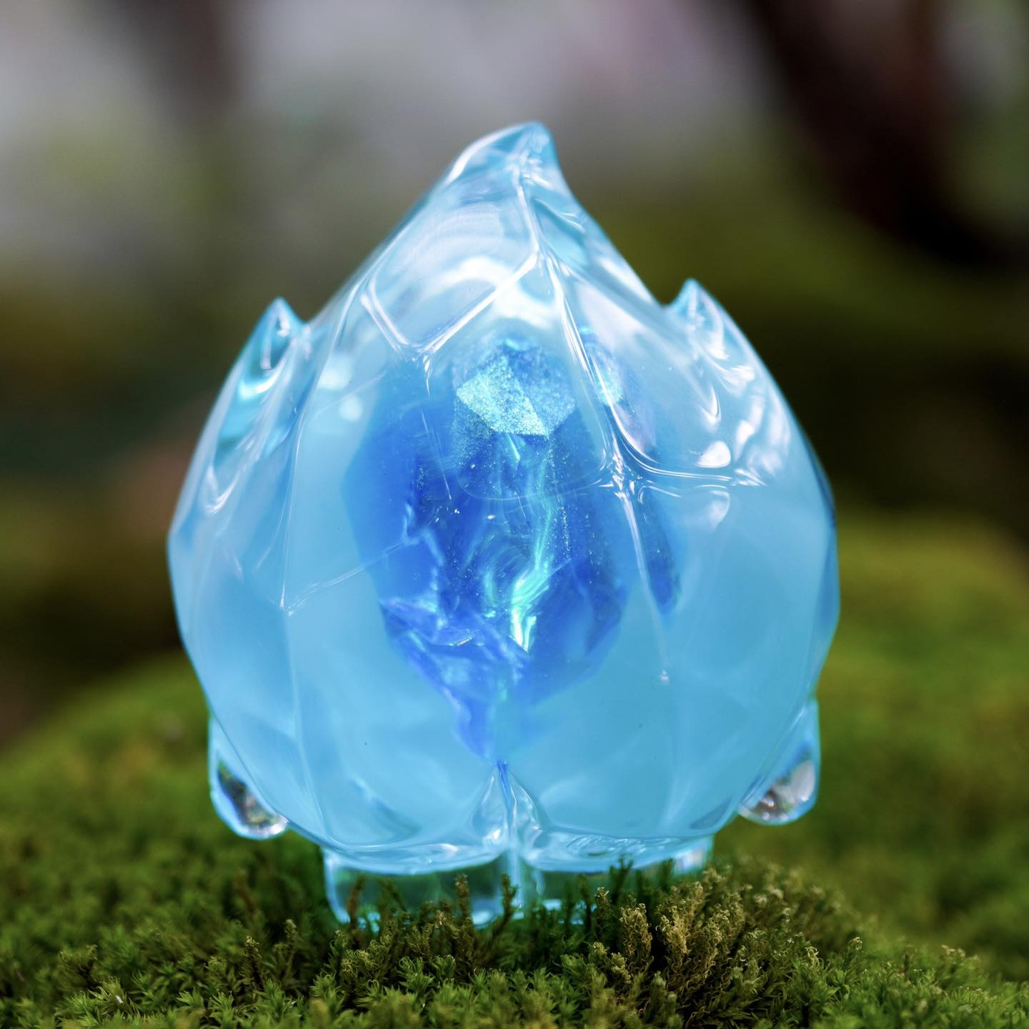 FLAMEY FROST - Blue Diamond by MUPA Toy: A translucent, ice-blue resin sculptural piece with a faceted core, displayed on moss. Limited to 50 pieces.