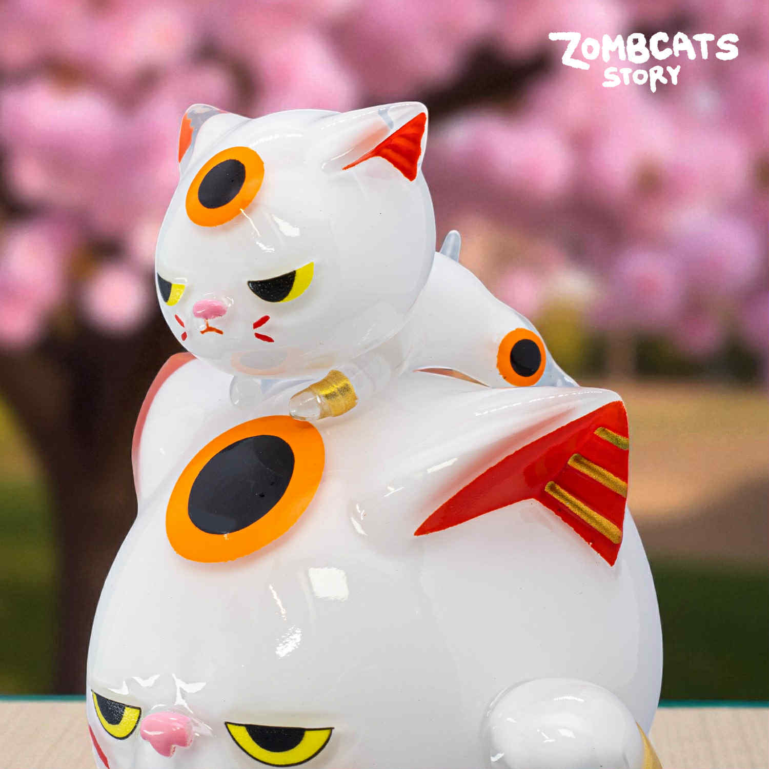 Zombcats Story - Grumpy Maneki LOTTERY features stylized white cat figurines with orange-ringed eyes, in glossy vinyl. Preorder for unique art toy collectors.