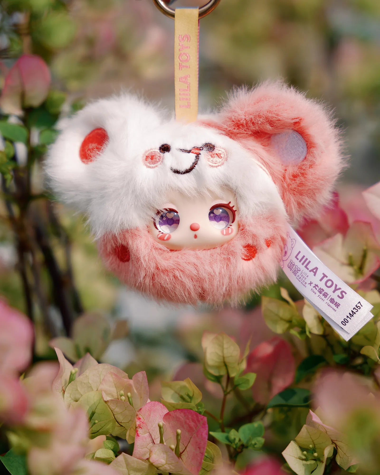 Liila’s Garden Tea Party Mini Plush Blind Box charm with anime-style face hangs among flowers, showcasing soft, fluffy design from LILA TOYS.