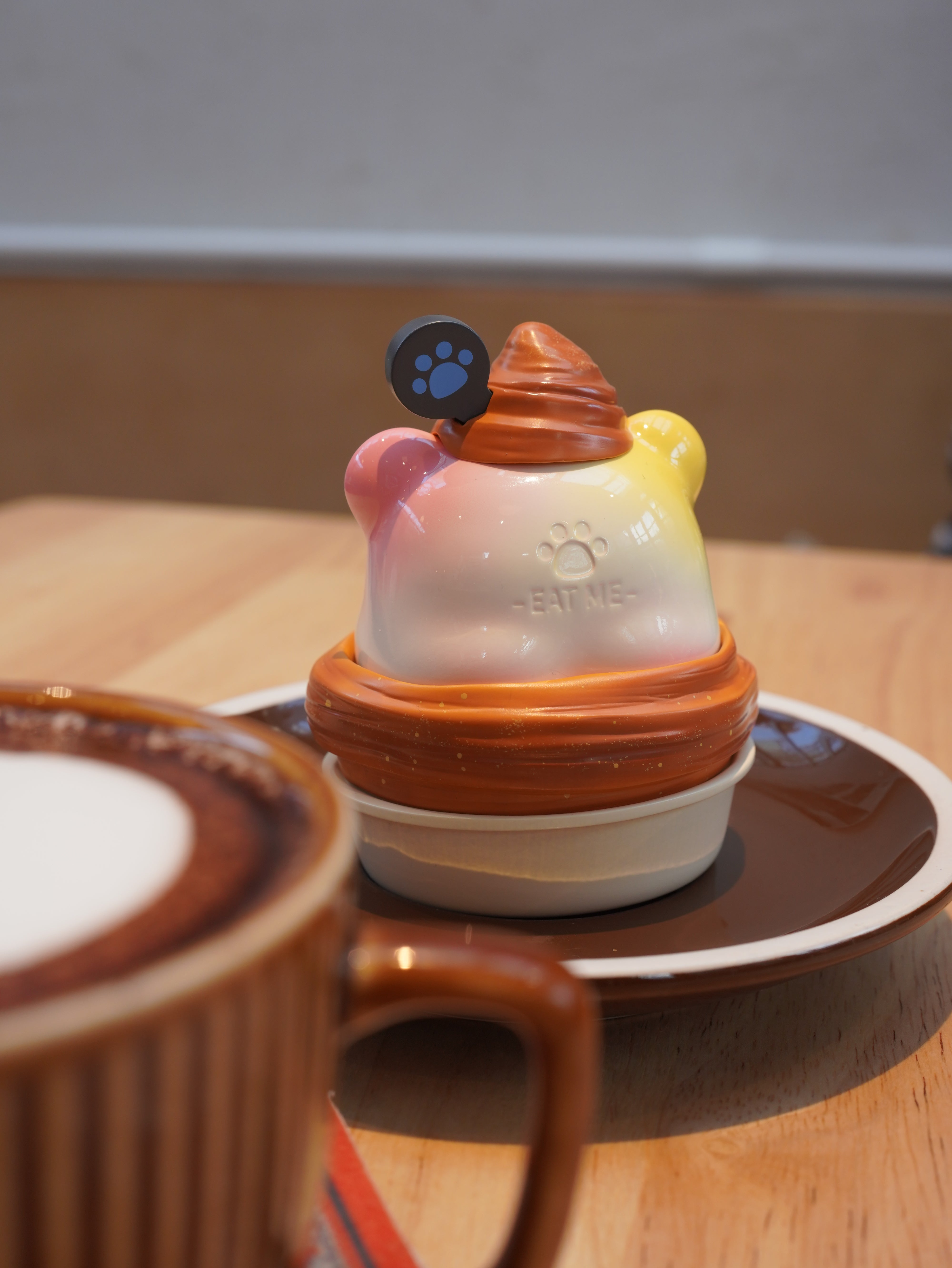 Croissant Han Han figurine on a plate with a cup and ceramic object, paw print on a hockey puck, close-ups of cup, toy, and handle.