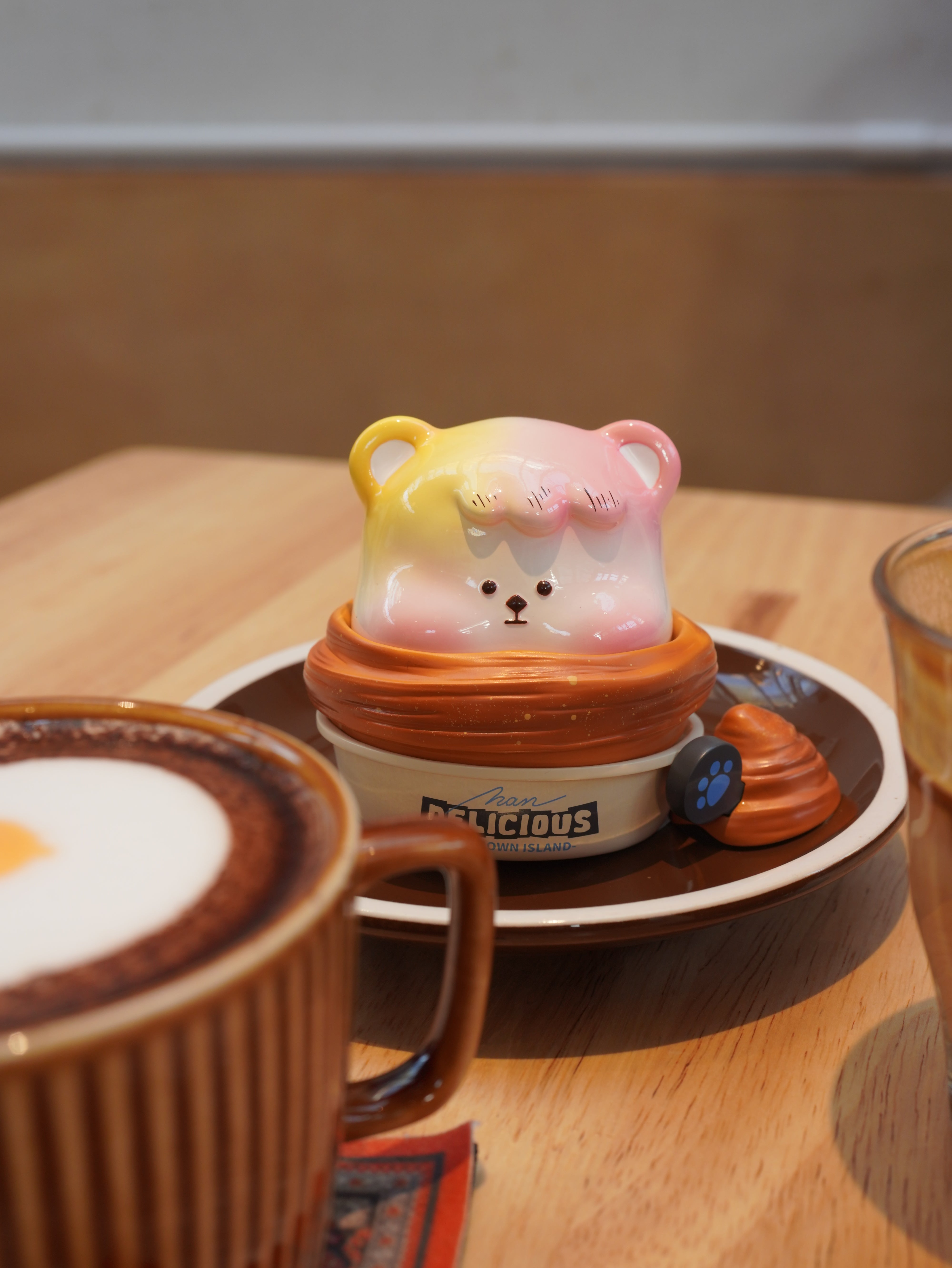 Croissant Han Han toy in coffee cup with saucer and toy bear on plate.