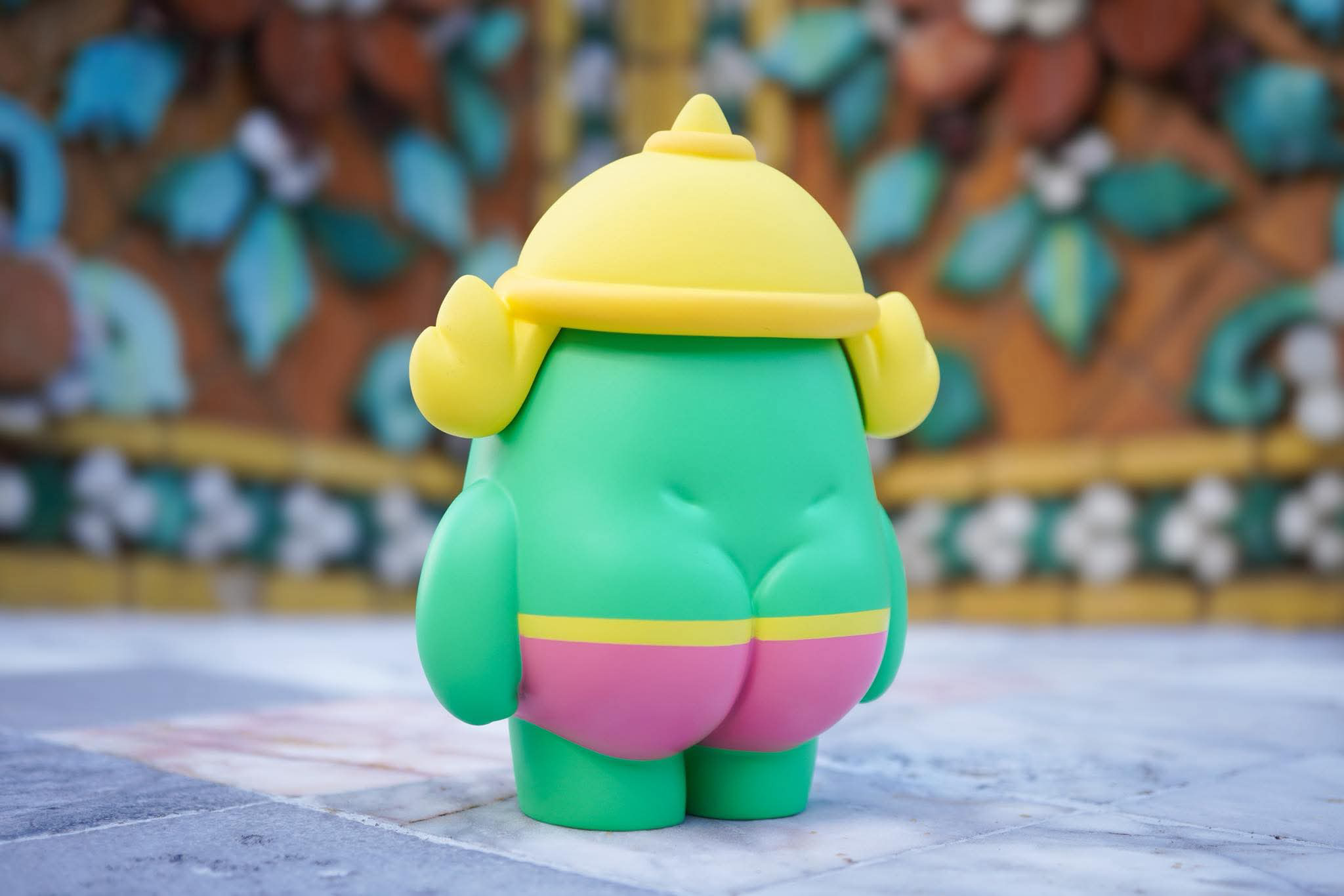 Mallow Yak by MUPA in bright green vinyl, wearing a yellow helmet and pink shorts, seen from behind. Preorder for November 2025, limited to 80 pieces.