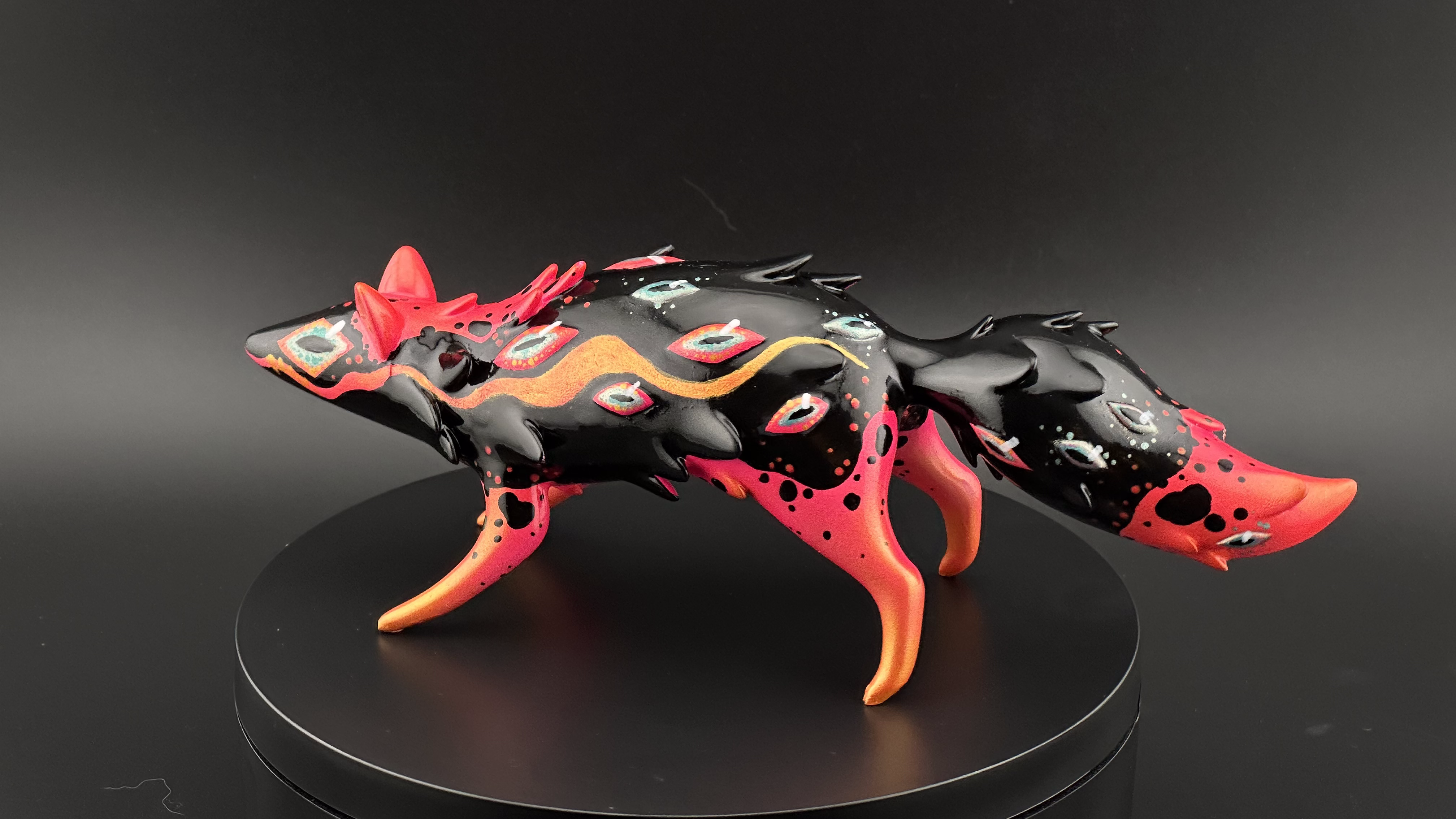 Whimsical, fox-like figurine, Whispers Screaming by Absolute Creature Vibes x Faunwood, with eye patterns and gold accents, on a black stand.