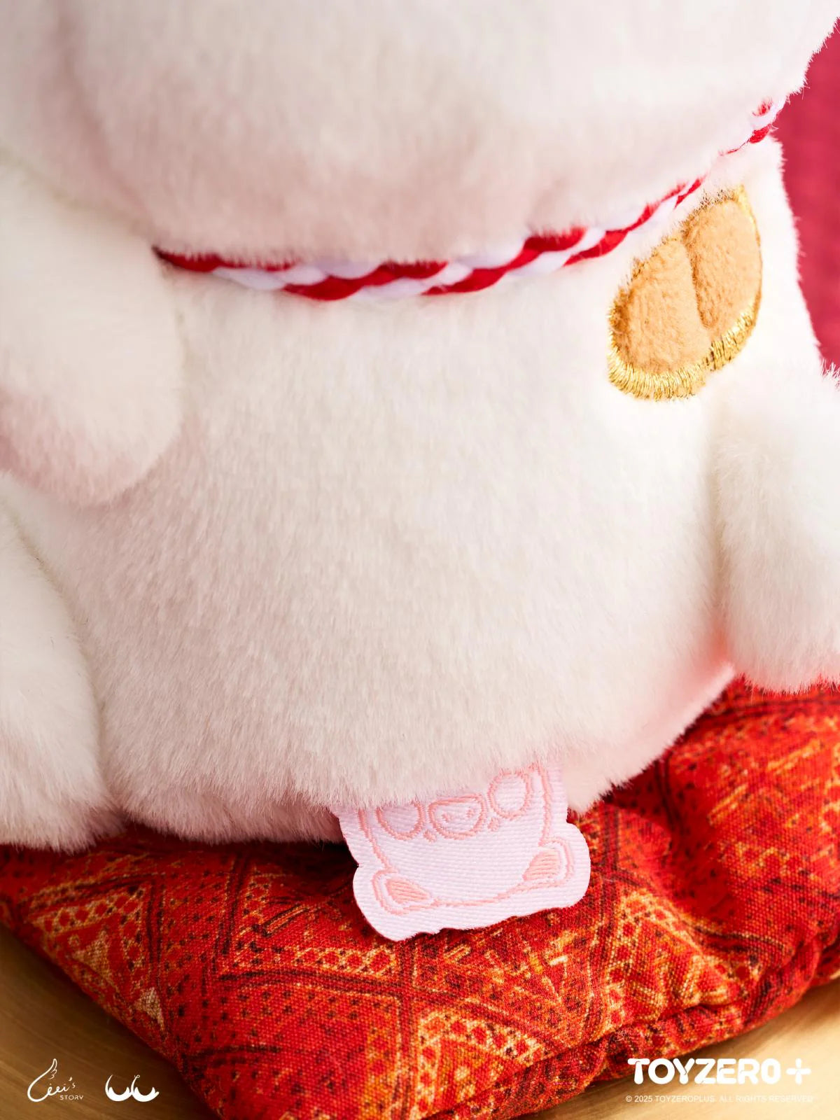 LuLu the Piggy - 'Lucky Meow On My Hand' plush toy, featuring a white maneki-neko with a braided collar, gold paw patch, on a red cushion.
