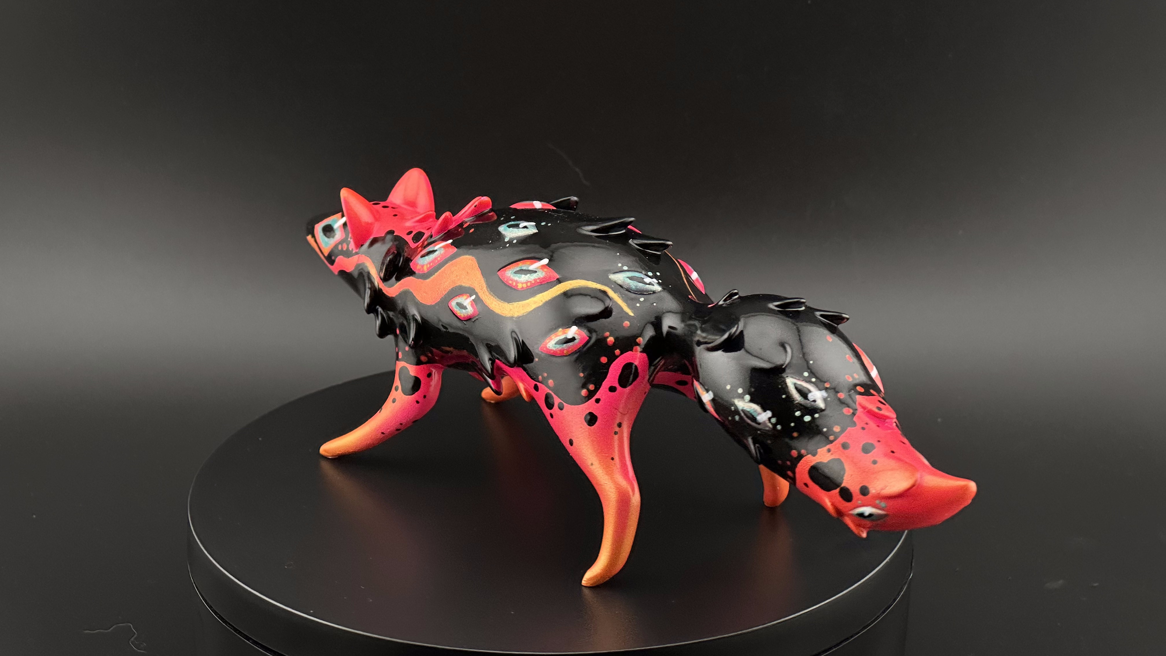 Fantasy creature sculpture by Faunwood, glossy black with colorful motifs, on display pedestal; part of ORACLE Group Show at Strangecat Toys.