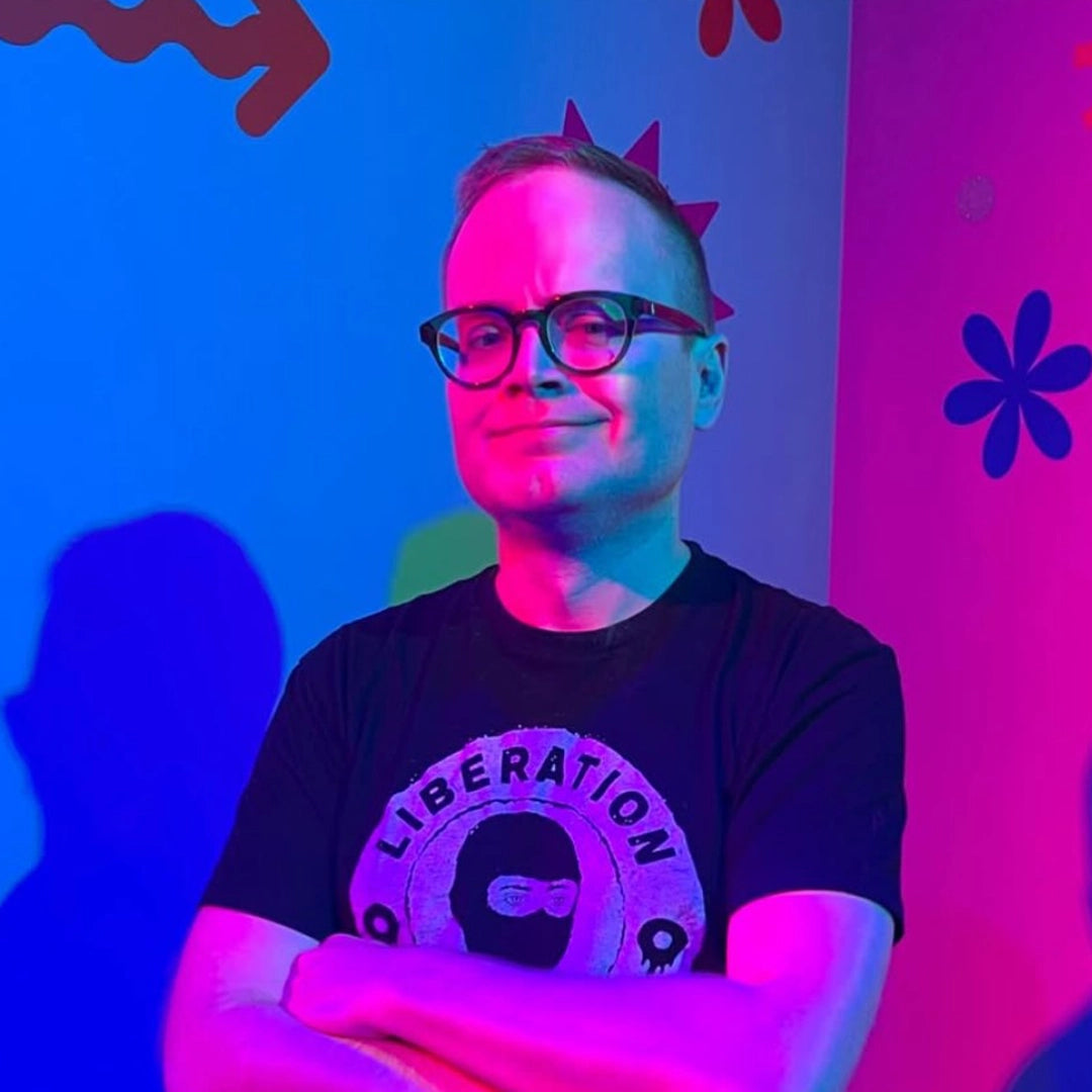 Middle-aged person in glasses, wearing a LIBERATION T-shirt, stands before abstract wall, promoting the Art Pickagram 3D Puzzle X Artist_03 Mr. Walters collaboration.