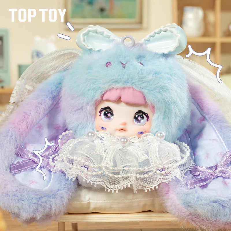 Nommi Baby Sweetheart Bunny Plush Blind Box featuring a doll's head in a pastel bunny hood, glittery eyes, and pearl-trimmed collar.