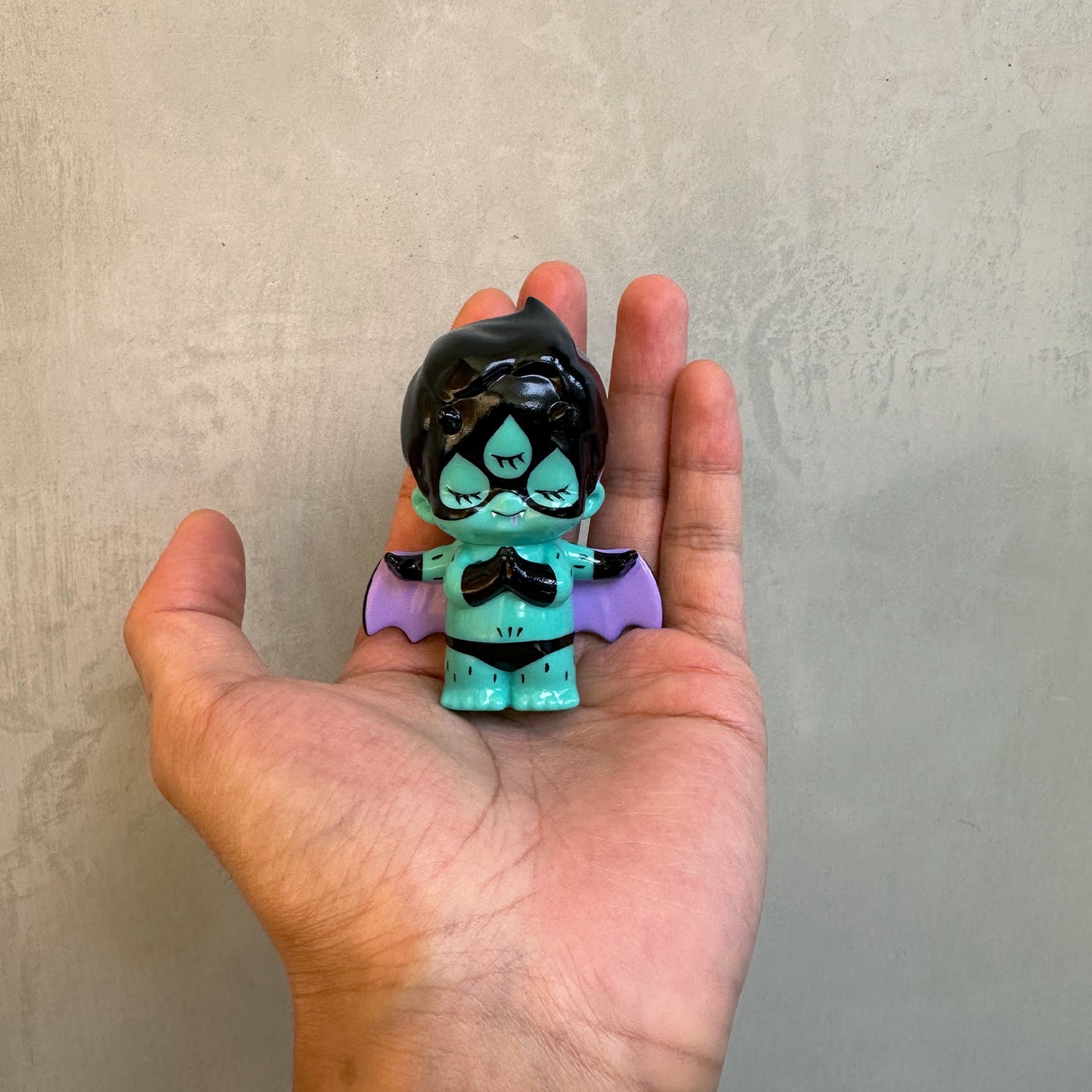 THE INSPECTOR DEDE BY ABAO, a mint-green vinyl toy with bat wings and glossy black head, held in a hand, perfect for collectors.