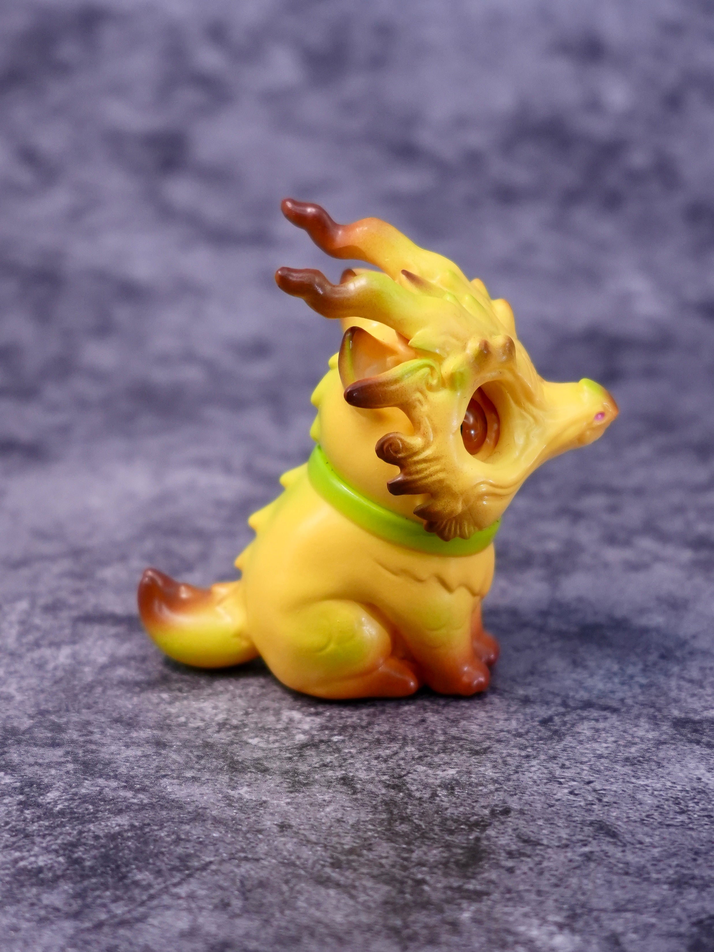 Banana Loong cat by HOTRU collectible figure, a cat-dragon fusion with antler-like horns, green collar, rotatable head, sitting on a gray surface.