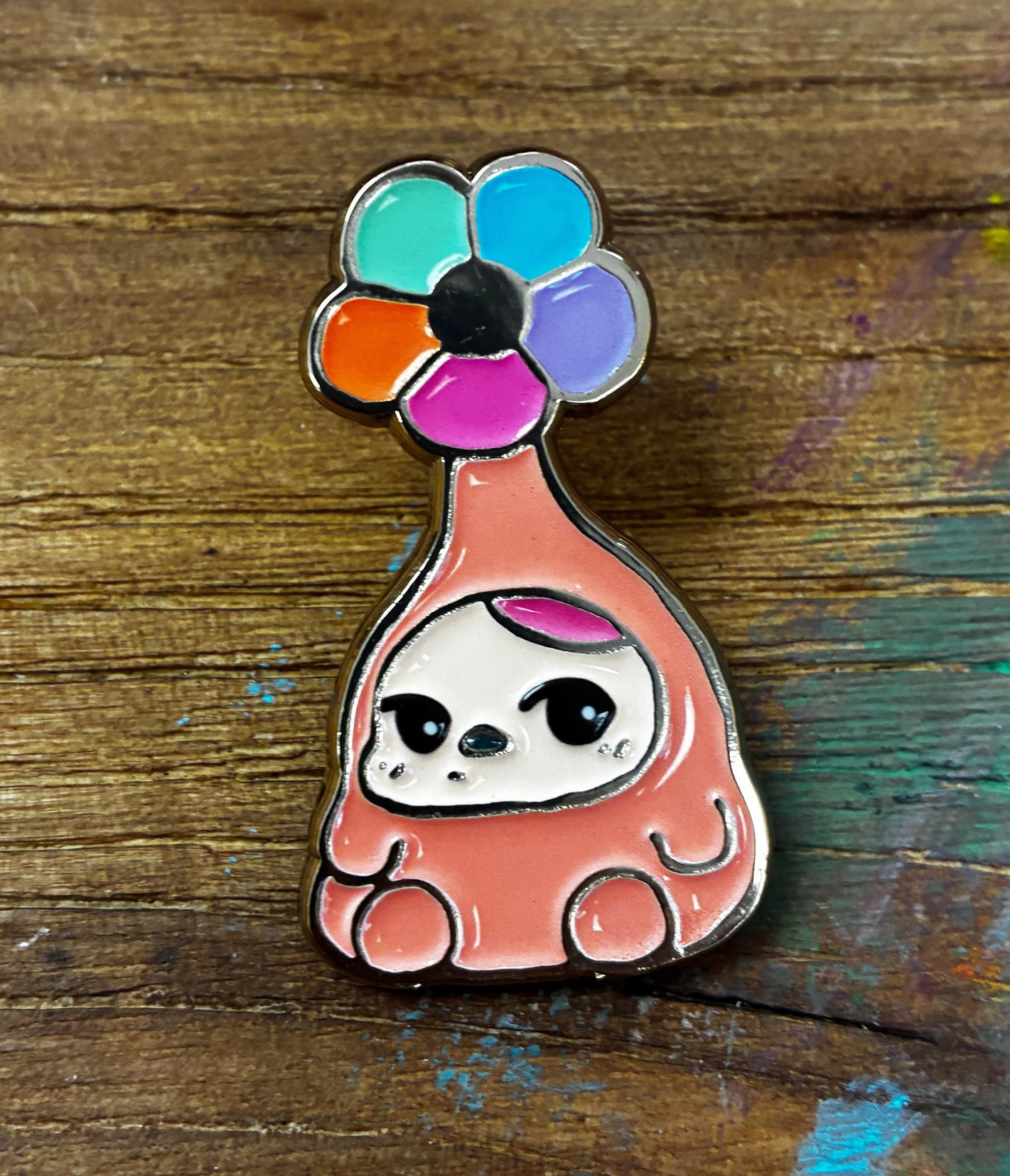 Bloom Pins by Pucky: Enamel pin of a chubby peachy-pink creature with cartoon eyes, featuring a vibrant six-petaled flower atop its head.