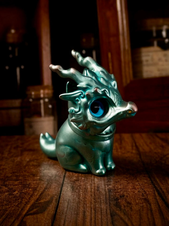 Bronze Longmi by HOTRU - Preorder: A metallic teal dragon-cat figurine with a rotatable head, oversized blue eye, and a magnetically attached mask on a wooden table.