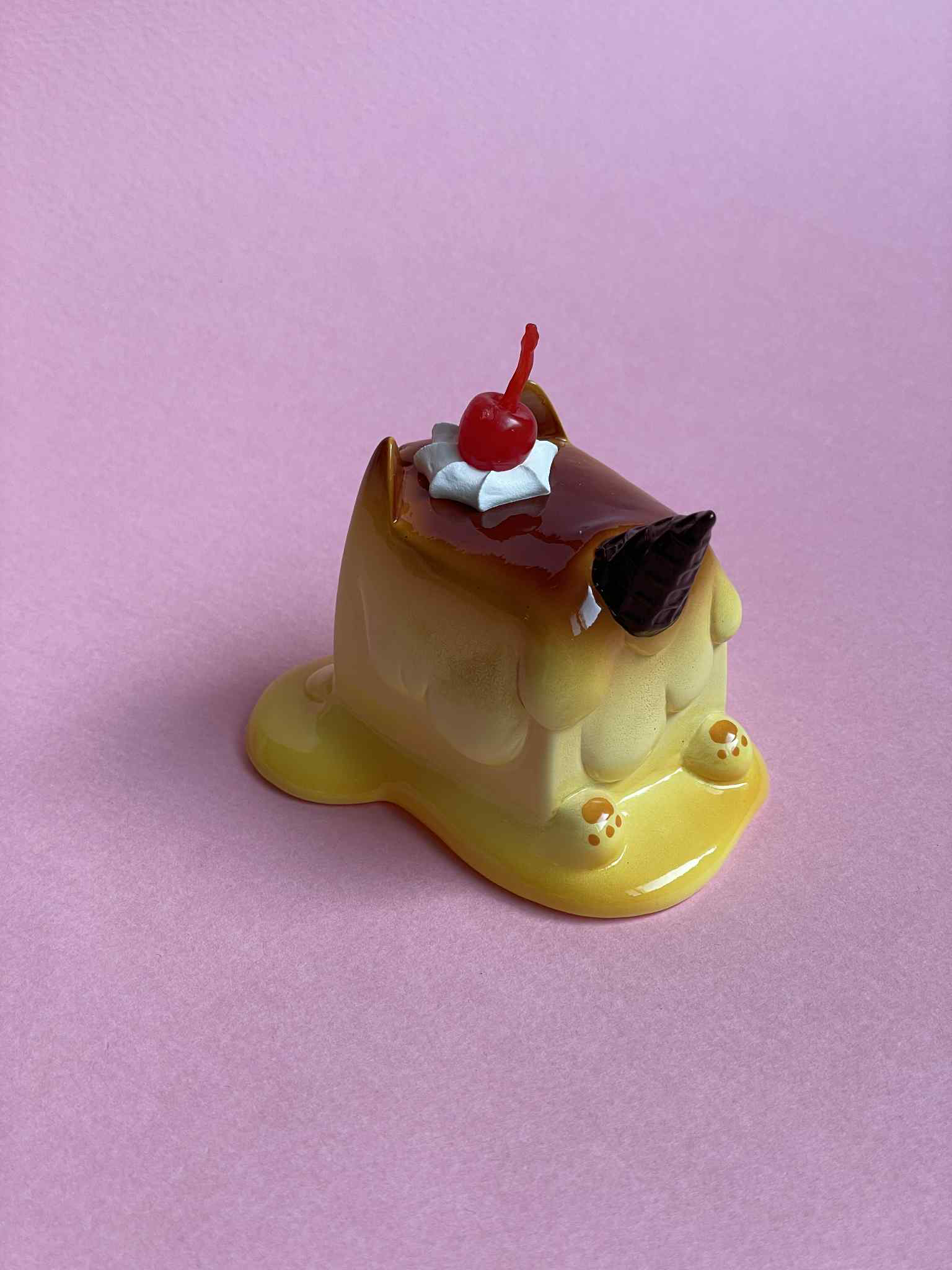 Pudding Cat by Rato Kim, a 6.5x7.5x5.7cm sofubi art toy, resembles a melting flan with whimsical details like a unicorn horn and cherry.