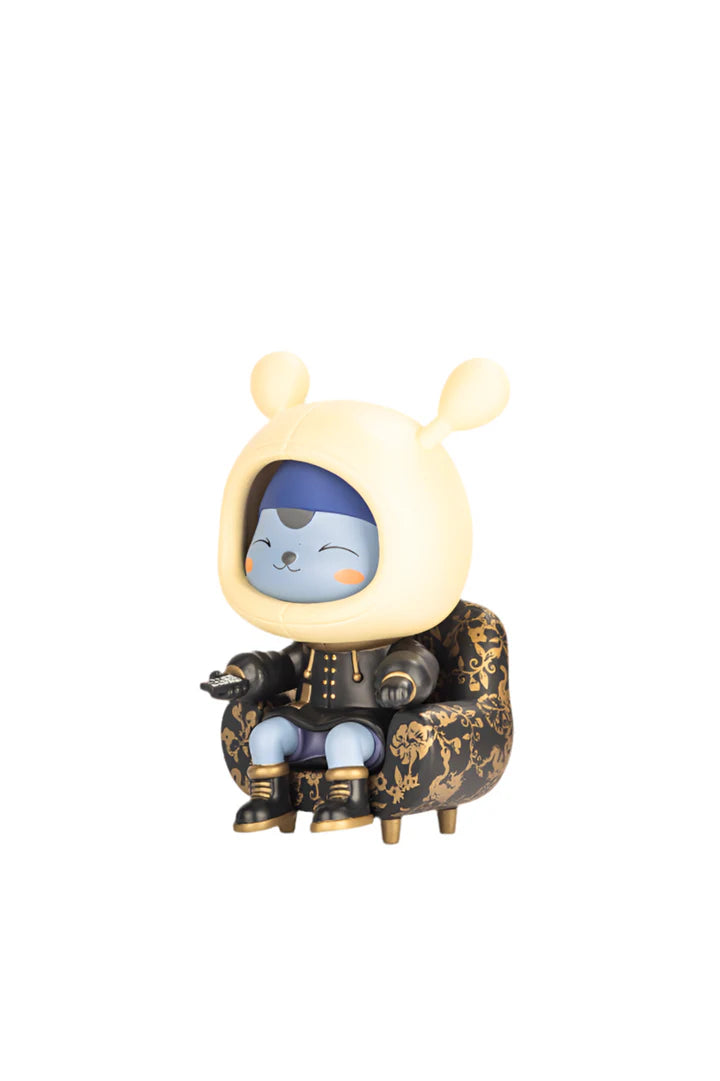 Napa - Obsidian: A vinyl toy of a blue-faced creature in a gold-patterned chair, embodying human culture, holding a remote, and smiling serenely. Limited edition.