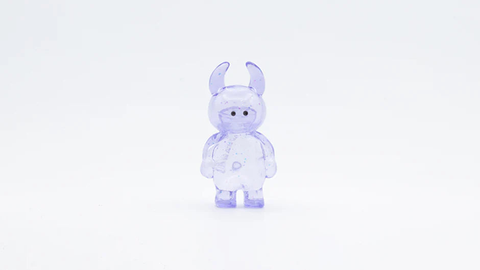 MINI UAMOU CLEAR LAVENDER GLITTER: A 4cm translucent figurine with a rounded body, stubby limbs, dot eyes, and horn-like ears, made of soft vinyl from Japan.