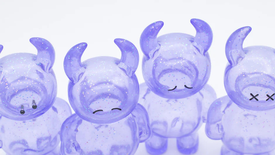 UAMOU CLEAR LAVENDER GLITTER features four small, translucent figurines with glitter, horn-like protrusions, minimalist faces, made of soft vinyl, 7cm tall.