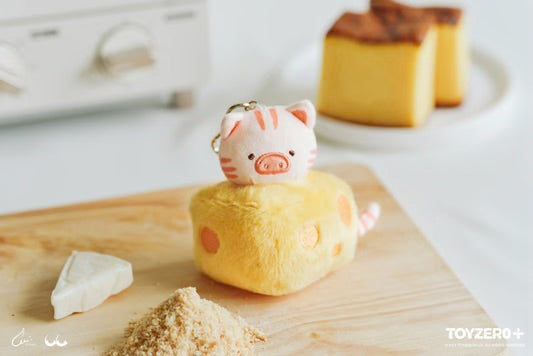Stuffed pig keychain on cheese block with dessert and dairy items.