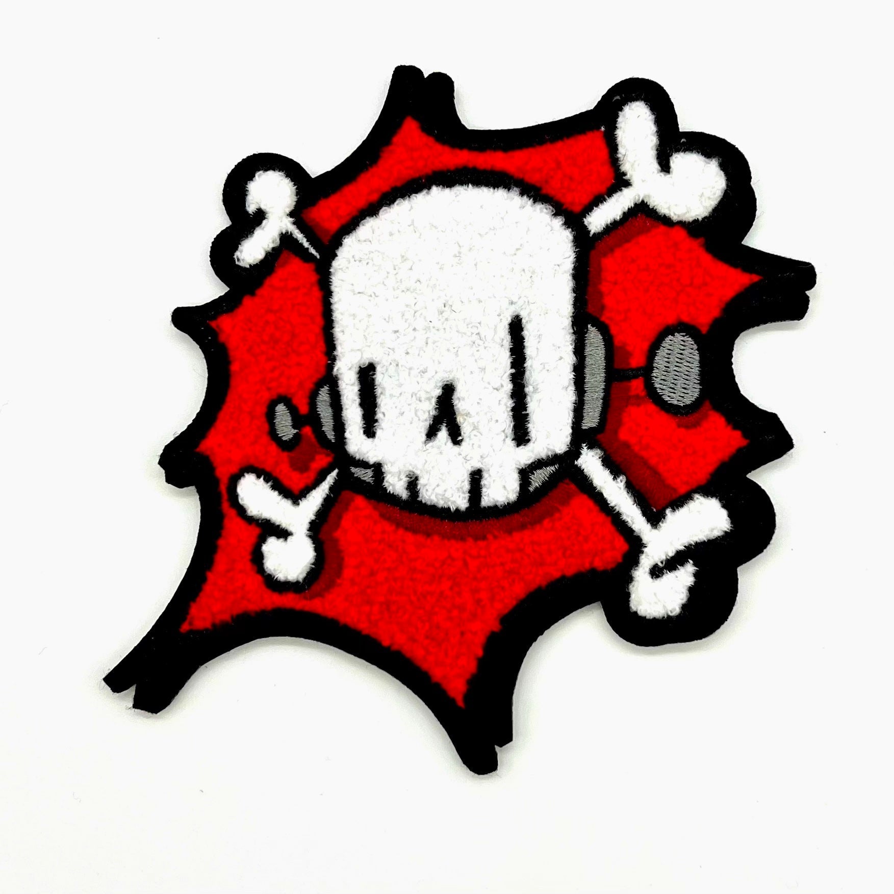 ChrisRWK Breakin' Through Chenille Patch featuring a cartoon skull and crossbones. 5 wide with iron-on backing, designed for art toy enthusiasts.