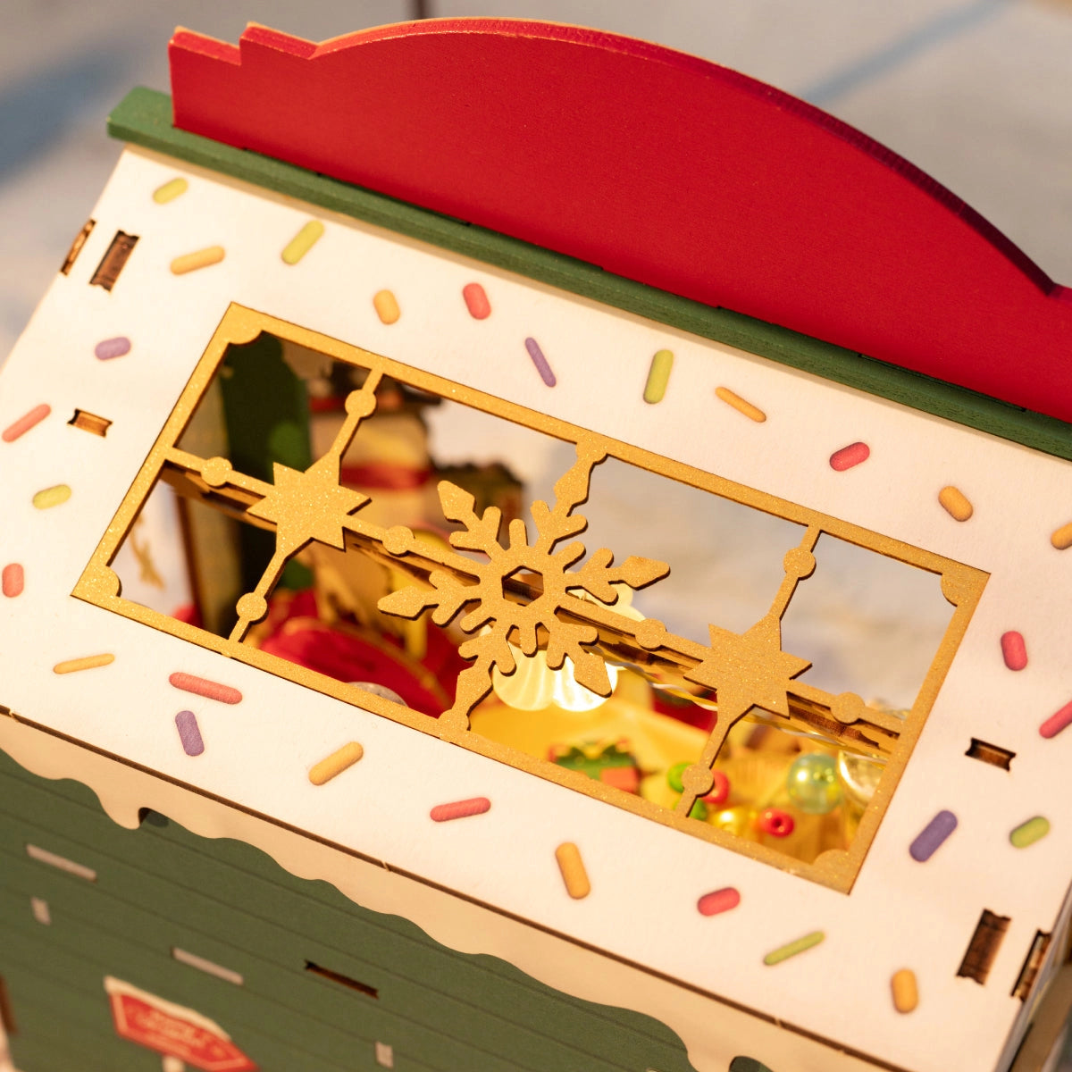 Rolife DIY Miniature House - Christmas Candy Stand DS043: A festive, painted wood gingerbread house with a miniature illuminated holiday scene visible through a gold snowflake window.