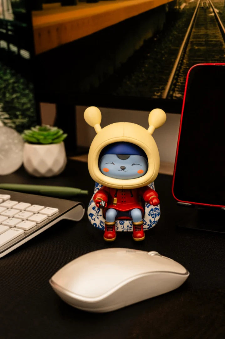 Napa - Porcelain: A vinyl figurine in a red outfit and yellow helmet, seated on a patterned armchair, with accessories like a mouse and succulent nearby.