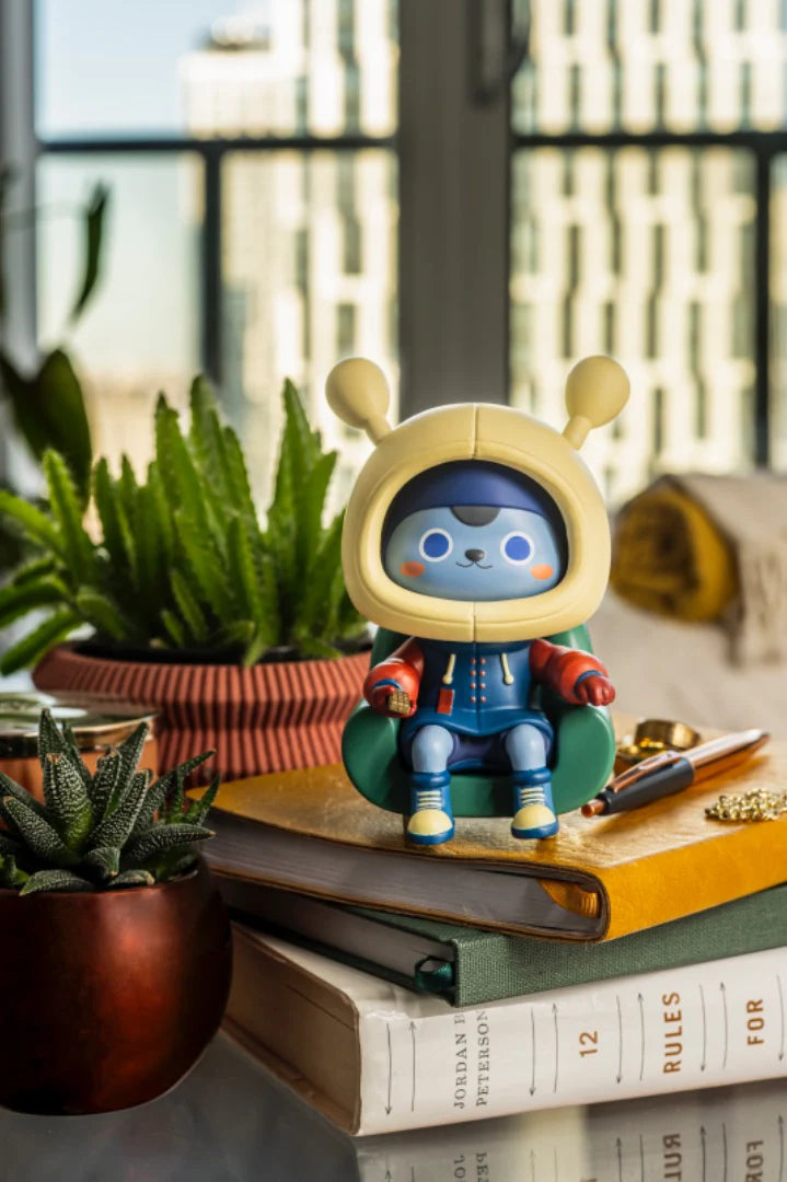 Napa Series One: A limited-edition blue figurine in a green armchair, inspired by human culture, perched on books with succulents nearby.