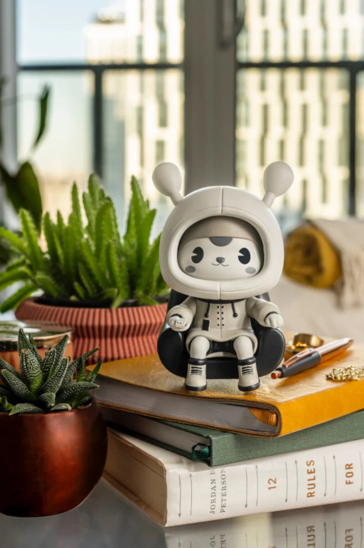 Napa - Retro, a vinyl art toy with a magnetic chair, sits atop an orange journal, surrounded by succulents and books in a bright, modern setting.