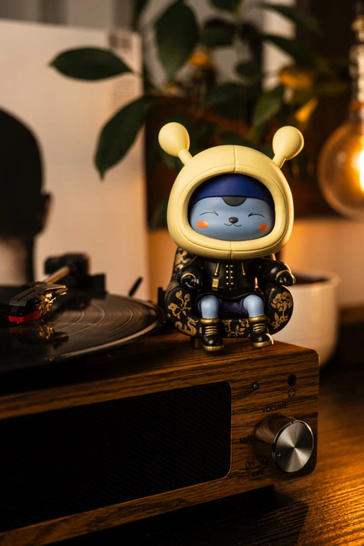 Napa - Obsidian vinyl figure on an ornate chair, seated on a wooden turntable with a spinning record, Edison bulb, and plant in the background.