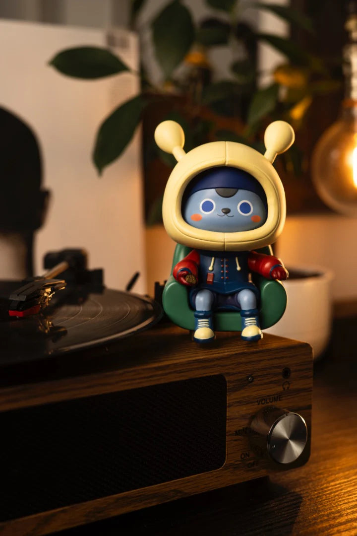 Napa Series One figurine: a blue alien-cat hybrid in a yellow helmet, seated with a game controller on a turntable.