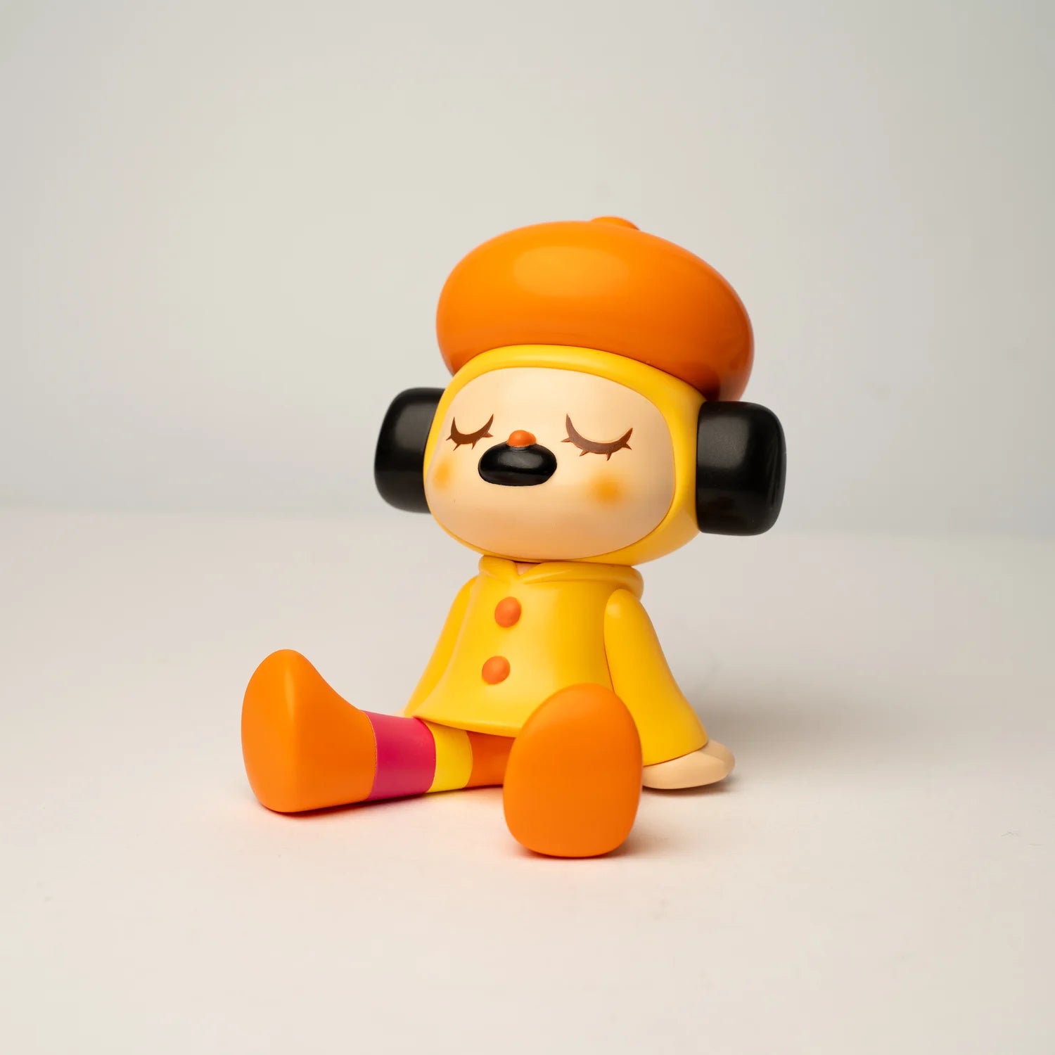 GREENIE OHIGEnoPON EDITION - Preorder: A small vinyl figure with orange beret and raincoat, earmuffs, closed eyes, and mismatched striped legs, perfect for collectors.