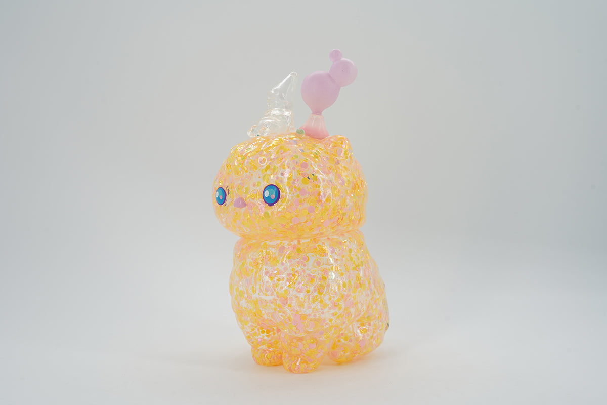 Mini Space Cat Bloom by Pucky, a yellow cat toy with a small pink bird on top, animal figure, cartoon.
