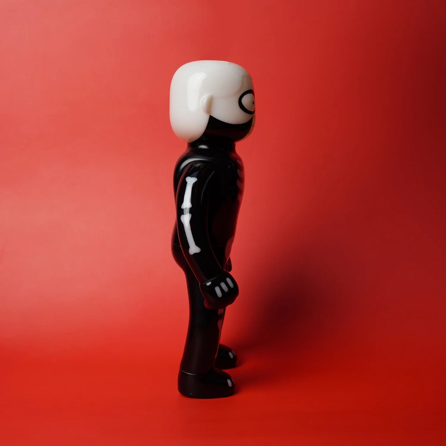 MR NOBODIES - SKELETON (GID GREEN) figurine, glossy black vinyl with white skeleton graphics, in profile against a red background. Preorder for a quirky art toy release.