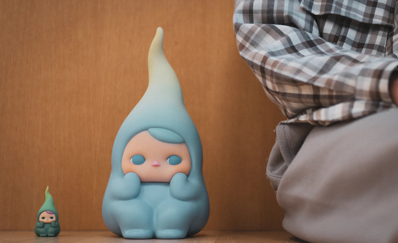 Big Beanie by Pucky: Two droplet-shaped vinyl figurines, featuring peach faces, on a wooden surface; the larger is 24cm. Partially visible person nearby.