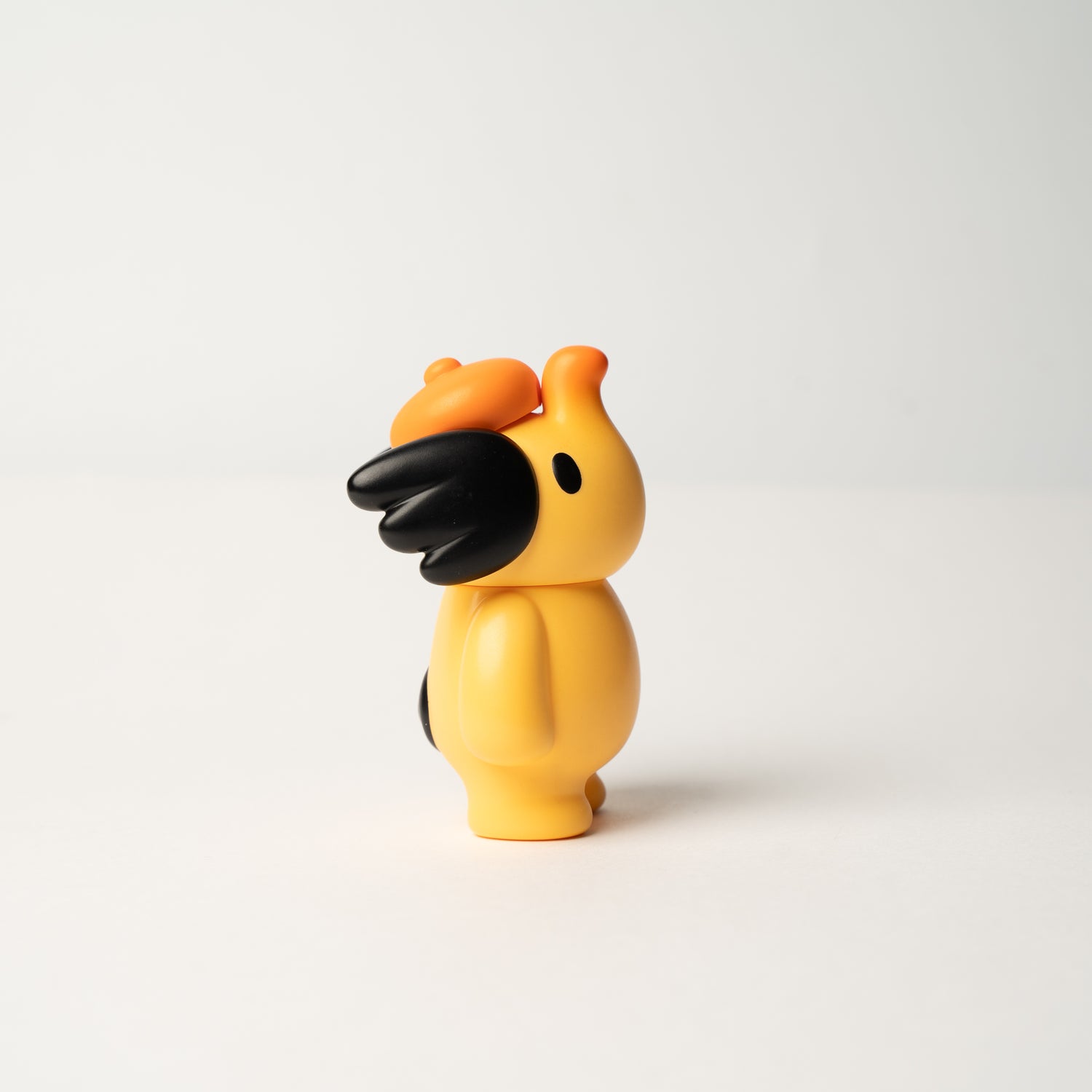 Elfie Here I Am! 100% OHIGEnoPON Edition vinyl toy with a yellow body, orange crest, and black accents, designed with a minimalist, cartoonish style.