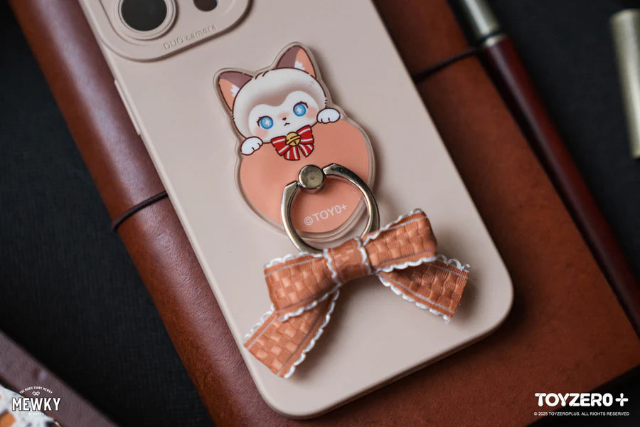 Cream-colored smartphone with Moffy's - Mewky Phone Ring Holder, featuring a Siamese cat design, on a leather notebook with pens beside it.