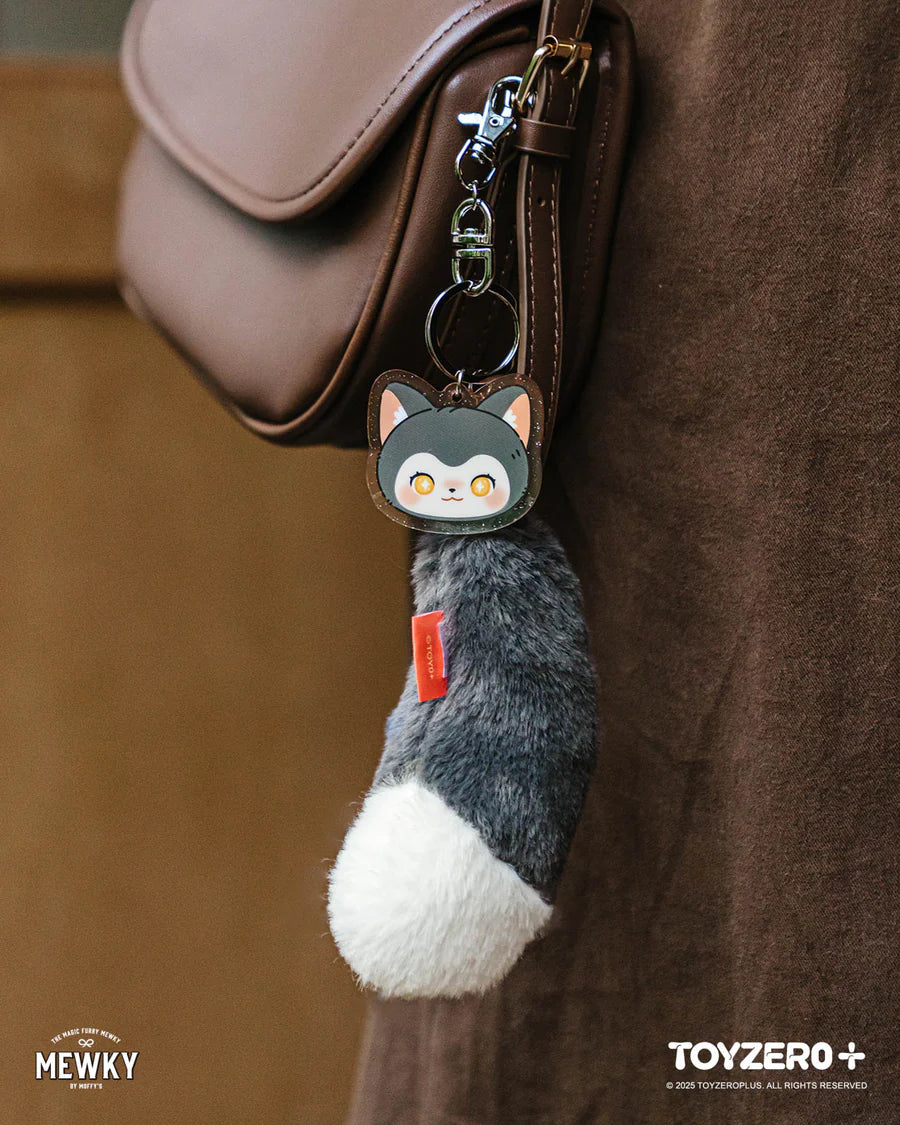 Brown leather-style shoulder bag featuring Moffy's - Mewky Cat Tail Keychain with a cartoon cat face and fluffy gray tail, perfect for adding charm.