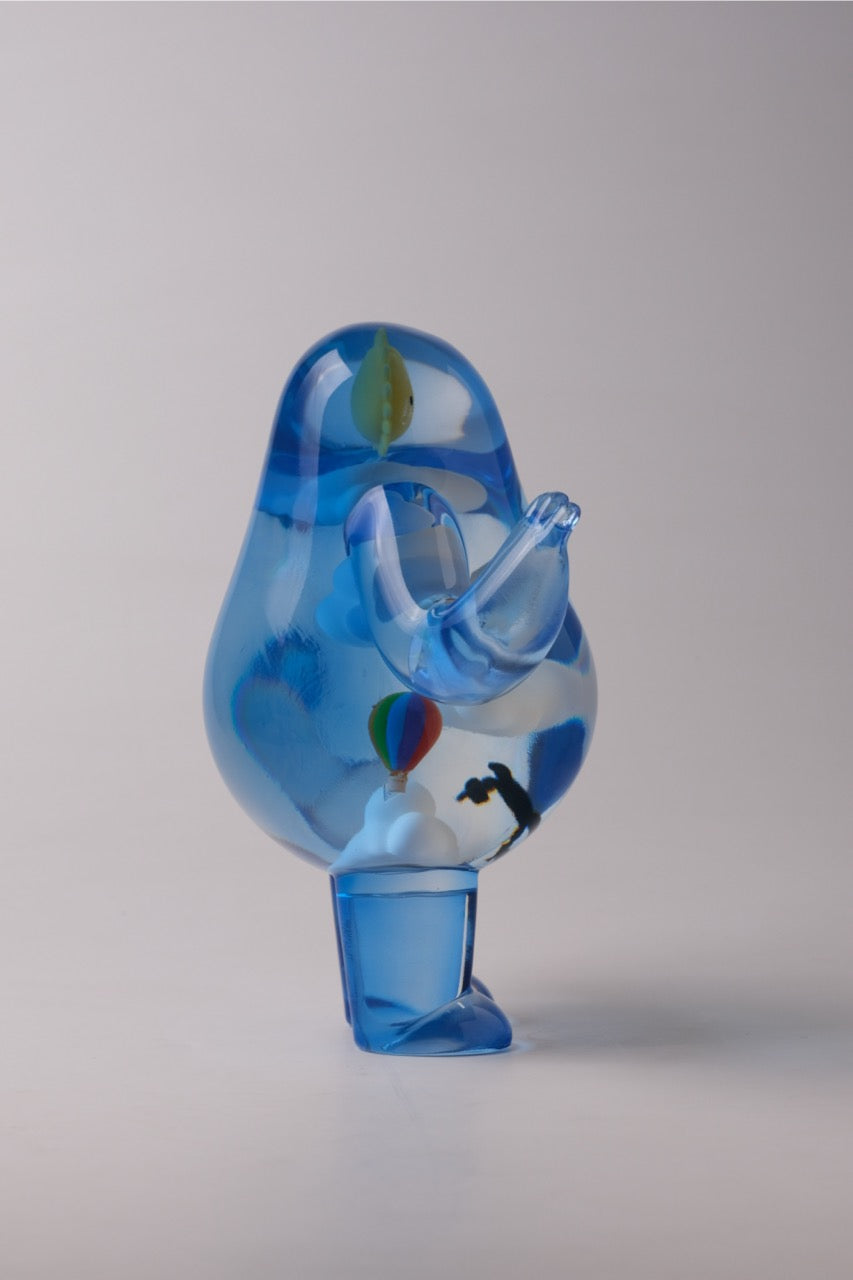 Sky Guy by Sad Salesman: A translucent-blue glass sculpture resembling an abstract bird with a cloud, hot-air balloon, and silhouette inside, featuring a distinctive beak and eye.