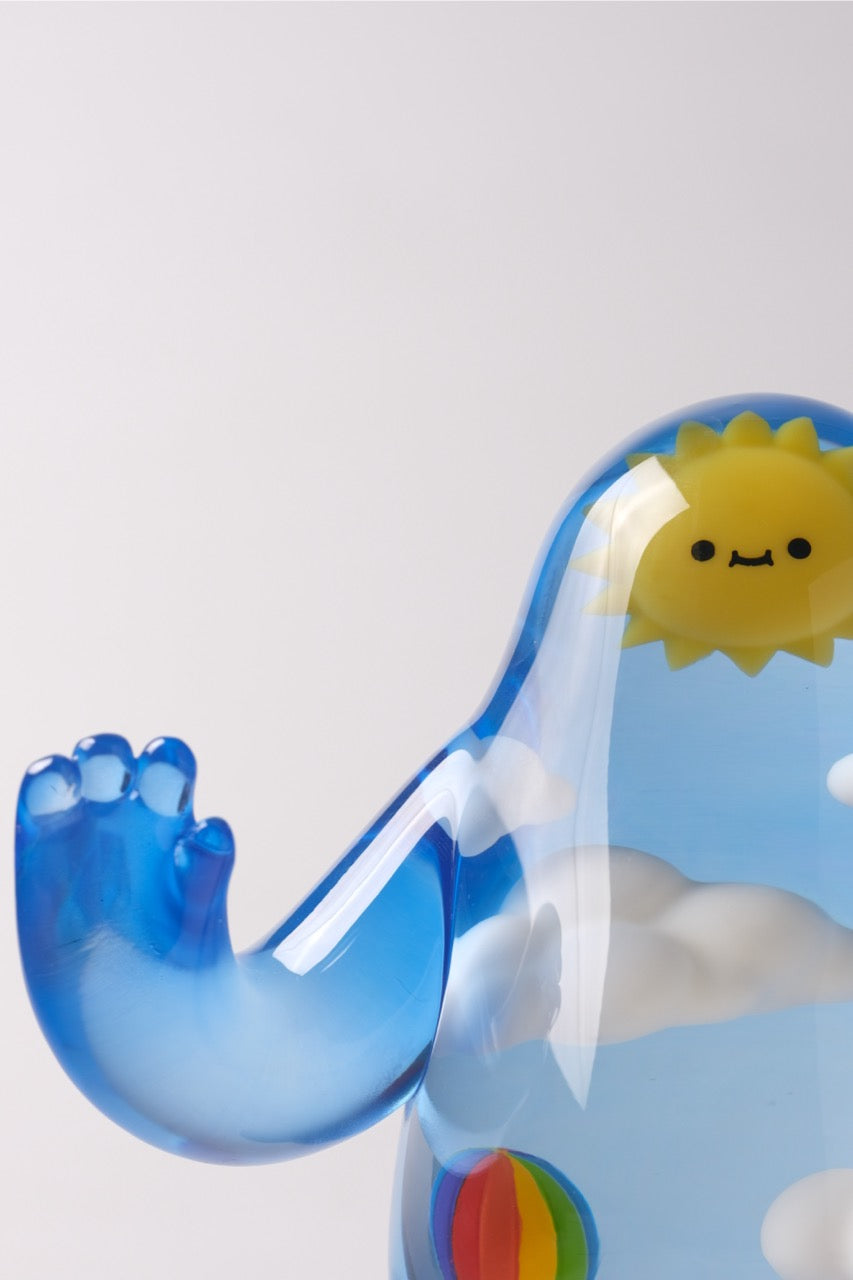 Sky Guy by Sad Salesman: A translucent blue art toy with cloud patterns, a smiling sun face, a rainbow detail, and a raised tentacle-like arm.