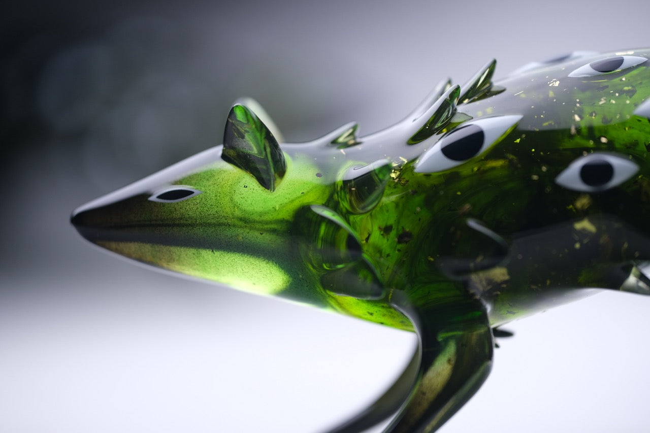Bogwalker Oracle by Faunwood: a 10cm stylized green glass sculpture of a shark-like creature, featuring unique eye motifs and limited to 100 pieces.