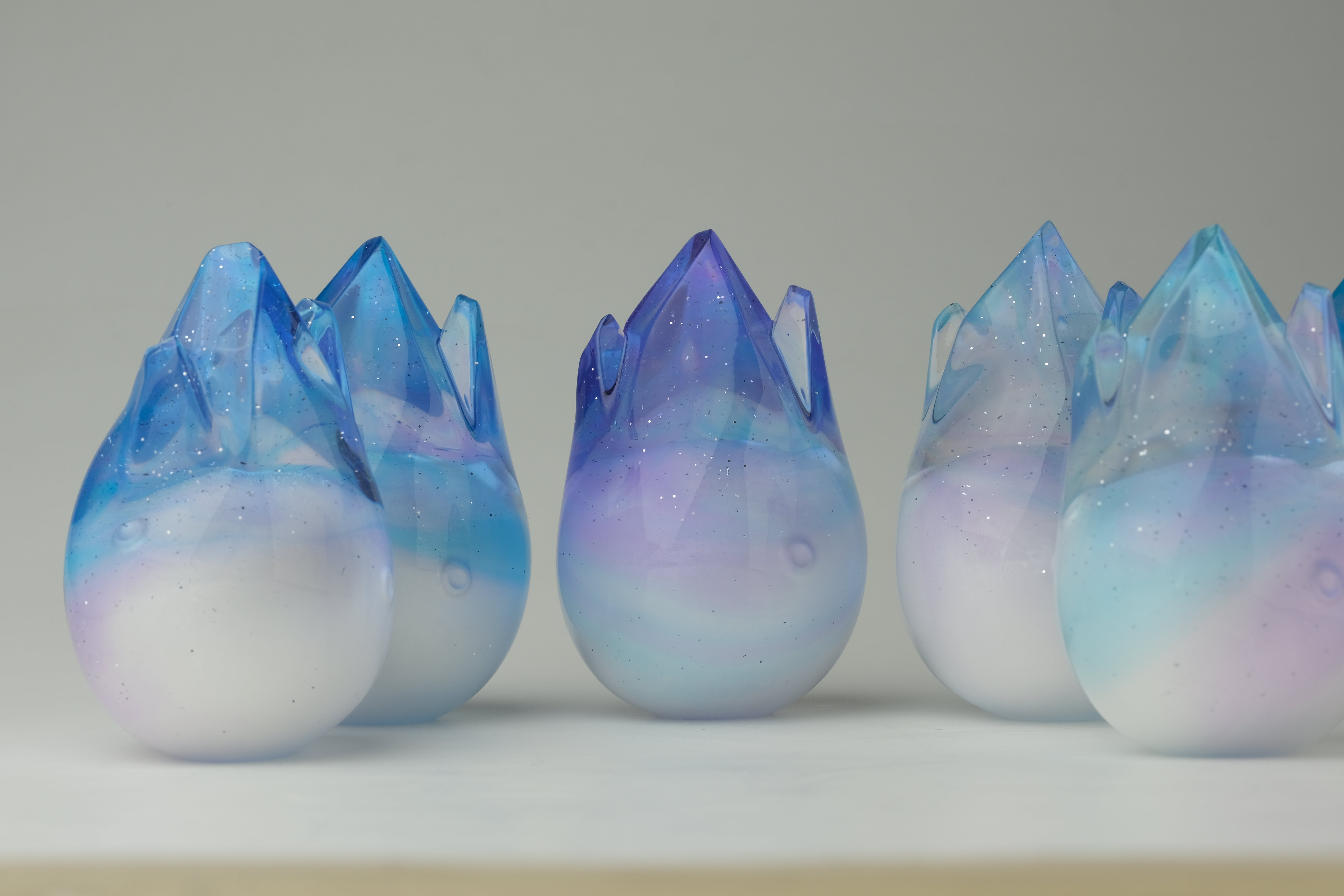 Aurora Cosmite by Yutoos: Hand-blown glass sculptures with opaque white bases and translucent blue-purple swirls, topped with jagged crowns. Limited edition of 50, each unique.