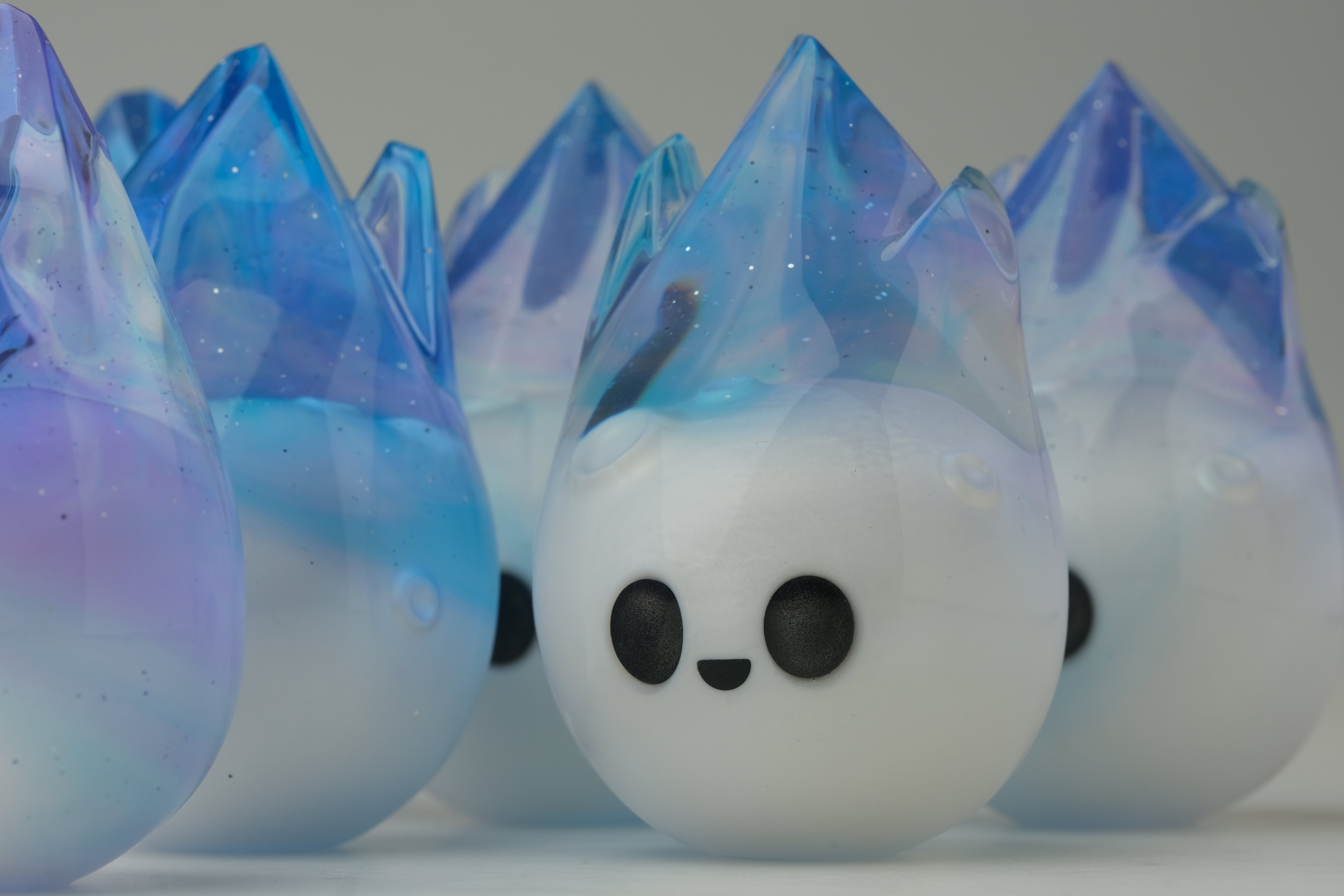 Aurora Cosmite by Yutoos: smiling ghost-like figurines with matte-white bases and iridescent crowns, 3.5 resin, unique art toys, edition of 50.