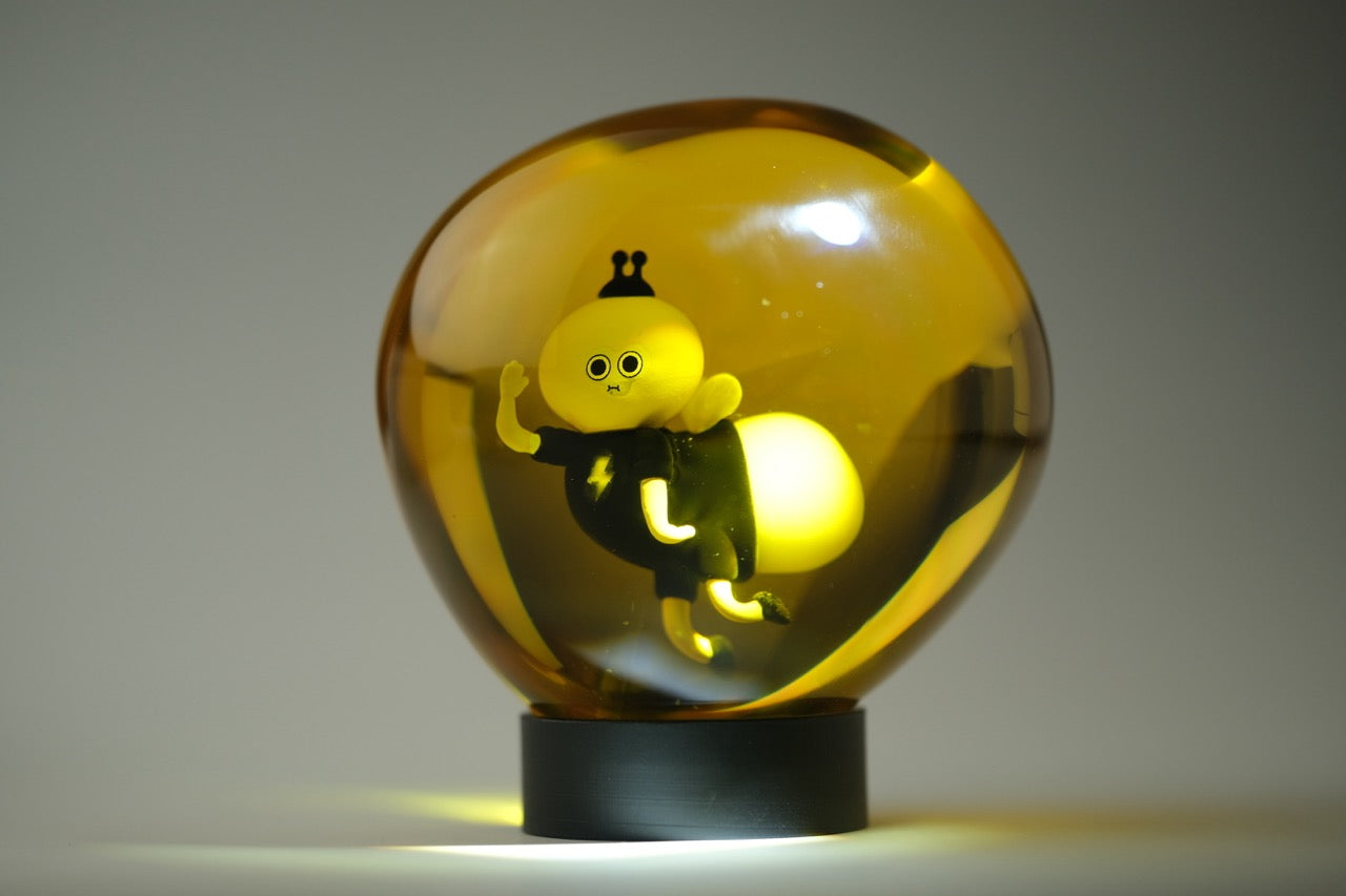 Lightning Bug by Sad Salesman: A glowing amber orb with a cartoon character inside, wearing a lightning bolt shirt, on a dark base.