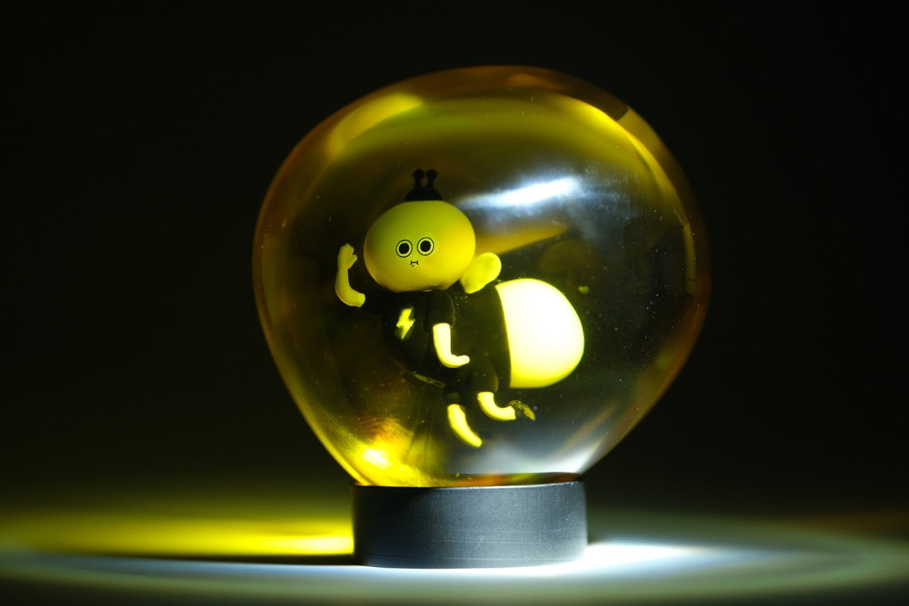 Lightning Bug by Sad Salesman: A glowing decorative glass orb lamp featuring a stylized insect with a lightning bolt emblem, part of the Bugs in Amber series.