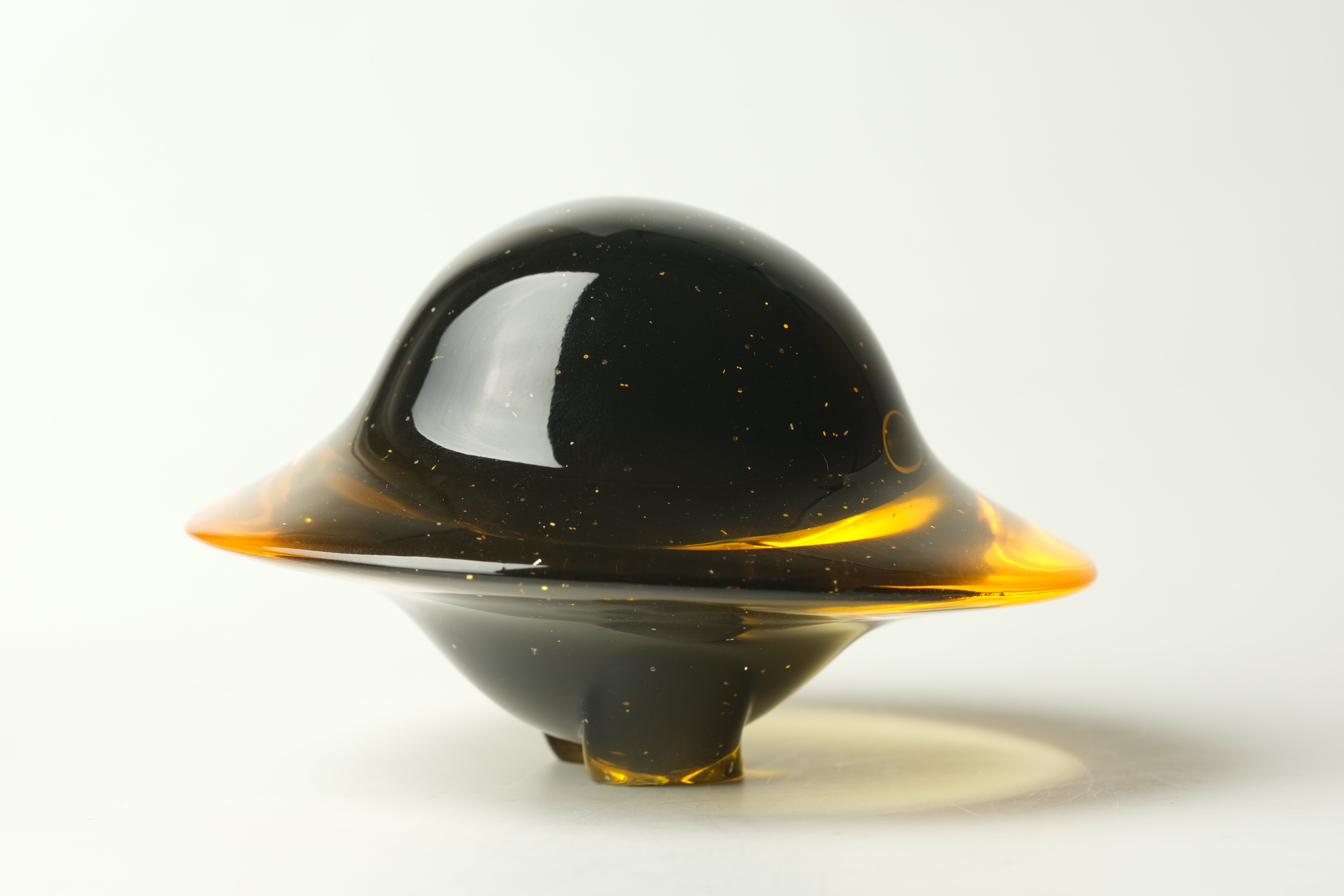 Darkmite by Yutoos, a 3.5 resin glass sculpture, resembles a flying saucer with a glossy black dome and translucent amber ring, unique edition of 50.